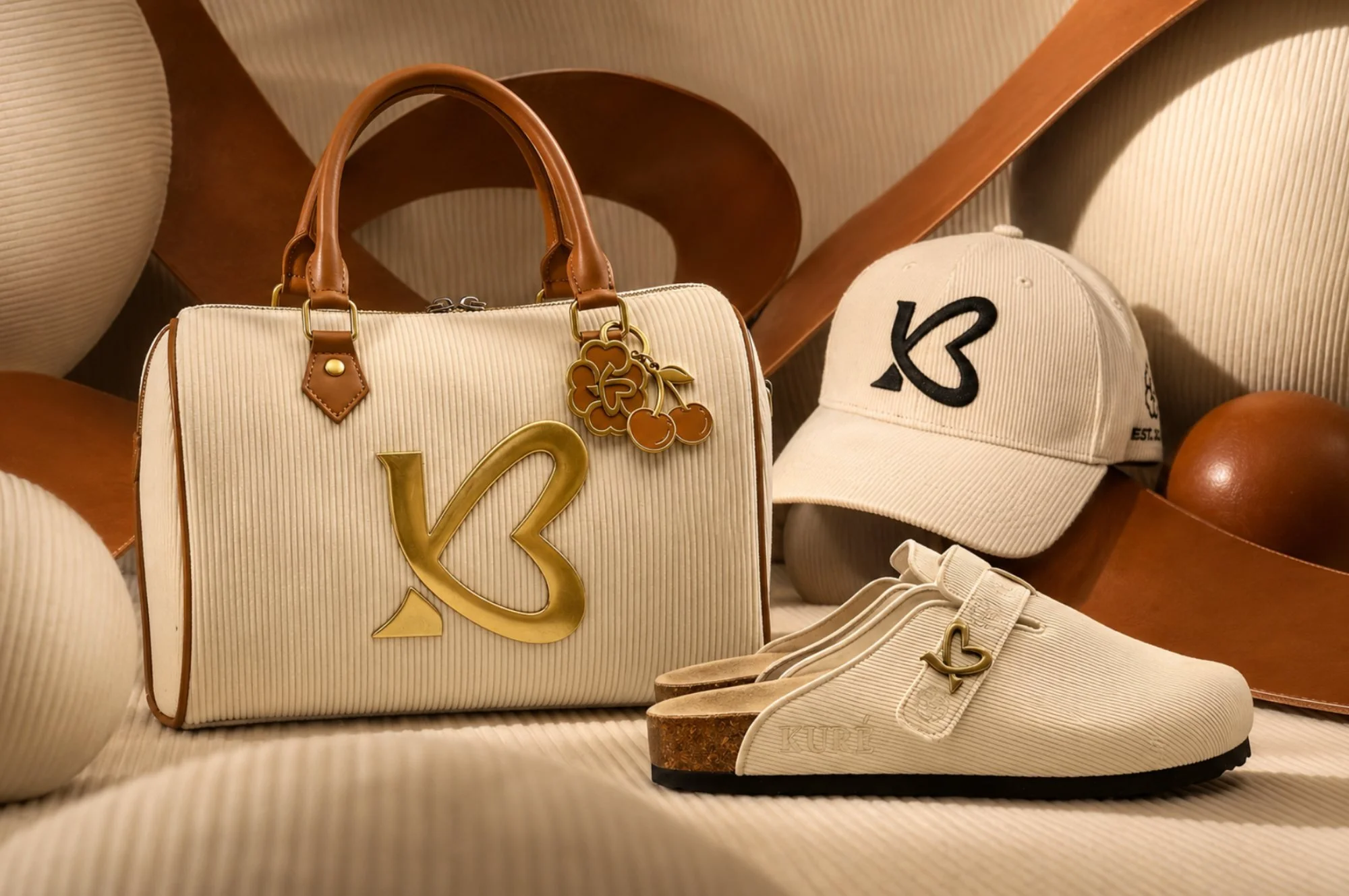 Cream handbag, cap and slip-on clogs with gold heart logos styled in a warm studio set