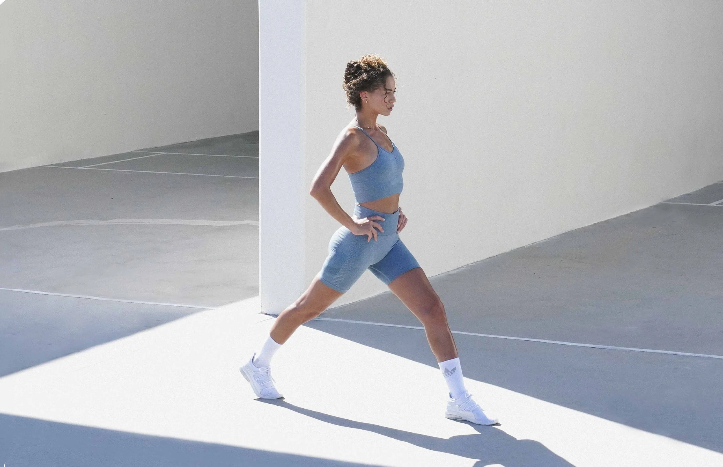 Female athlete in a blue Puma activewear set walking through white architecture in hard sunlight, Los Angeles