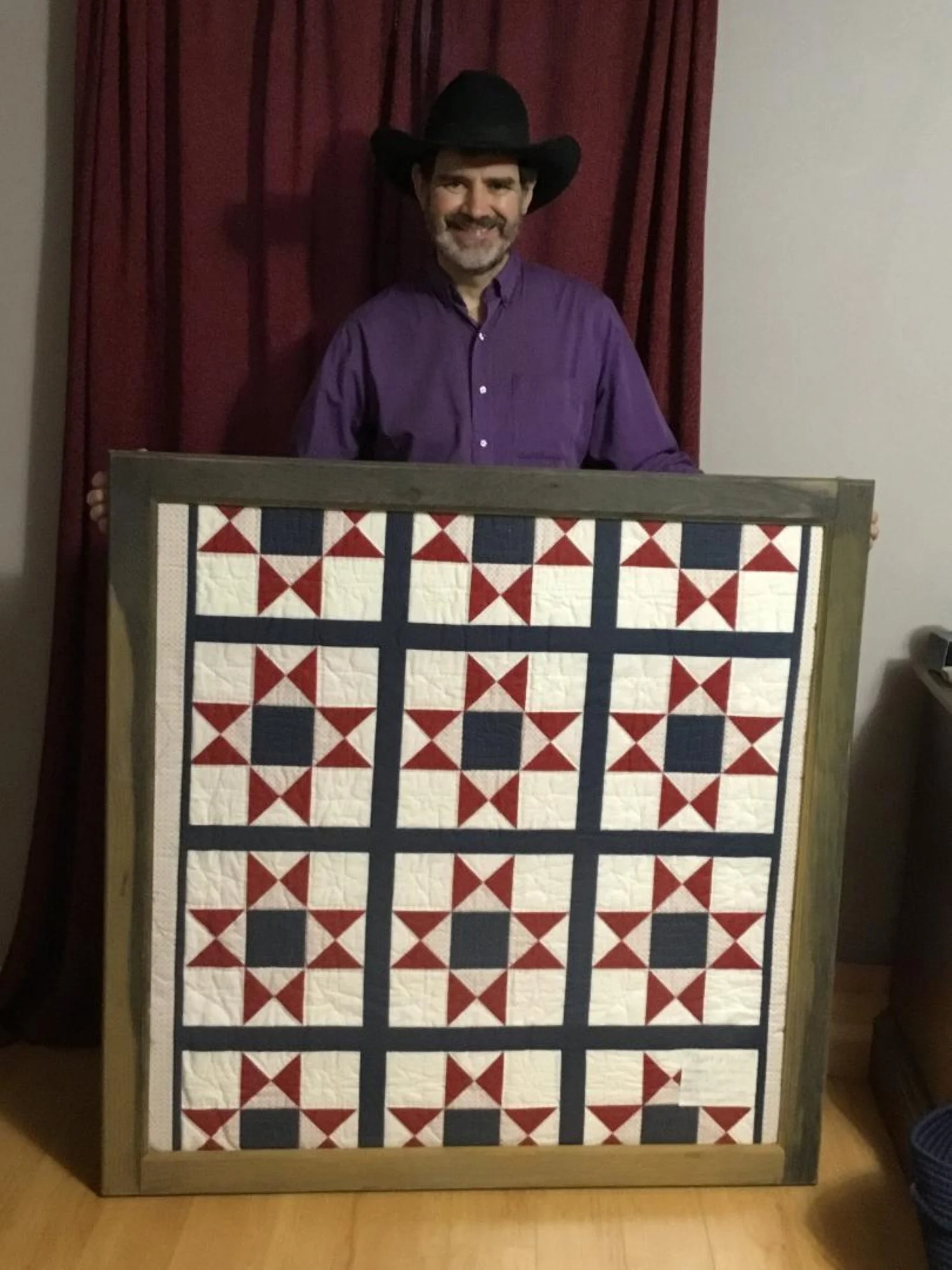 William Gajda holding up a framed quilt