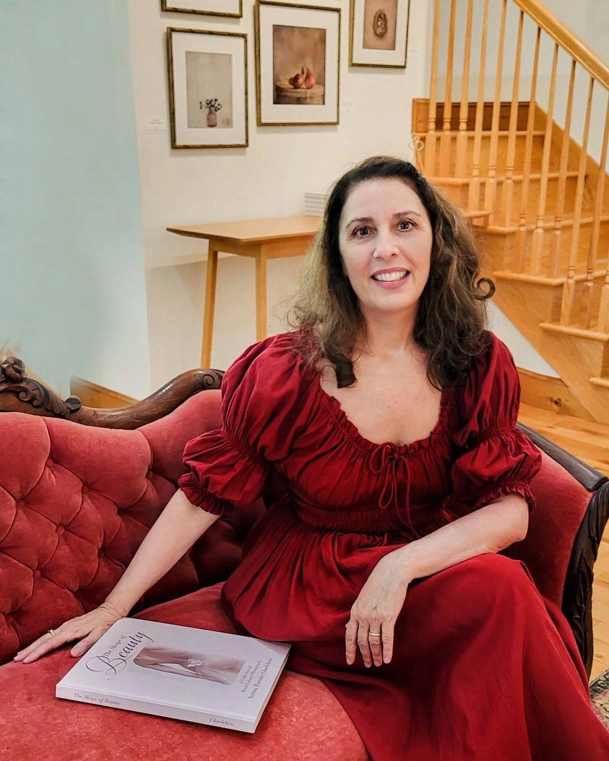 Serena Parente Charlebois smiling sitting on a red couch with a copy of her book "The Magic of Beauty"