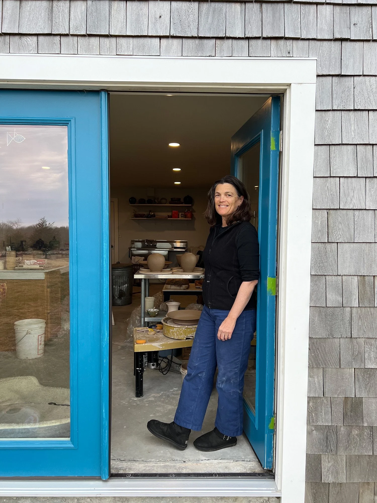 Cali Almy standing in the doorway of her studio with pottery behind her