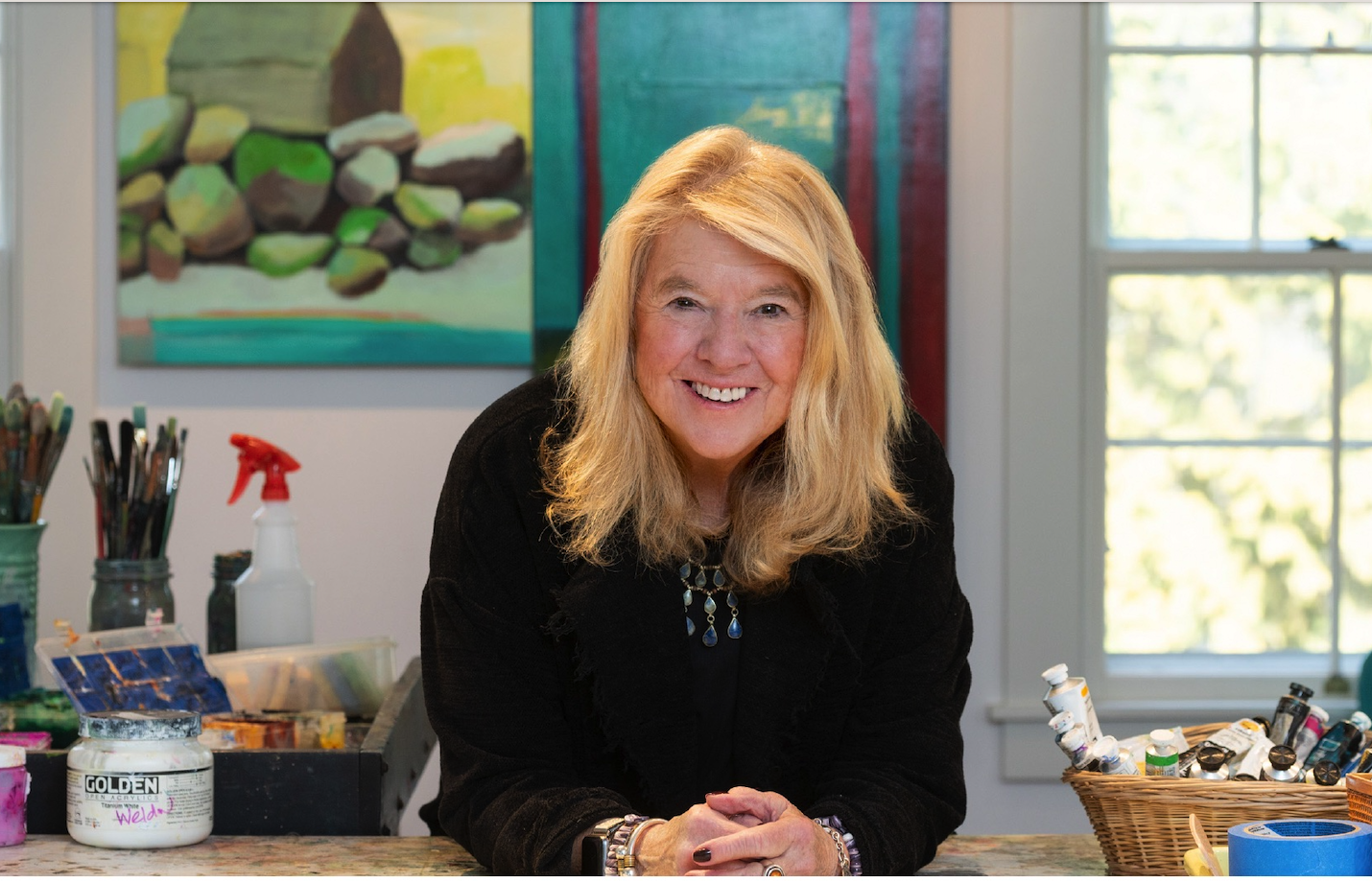 Wendy Weldon smiling at the camera in her studio with art supplies on either side of her