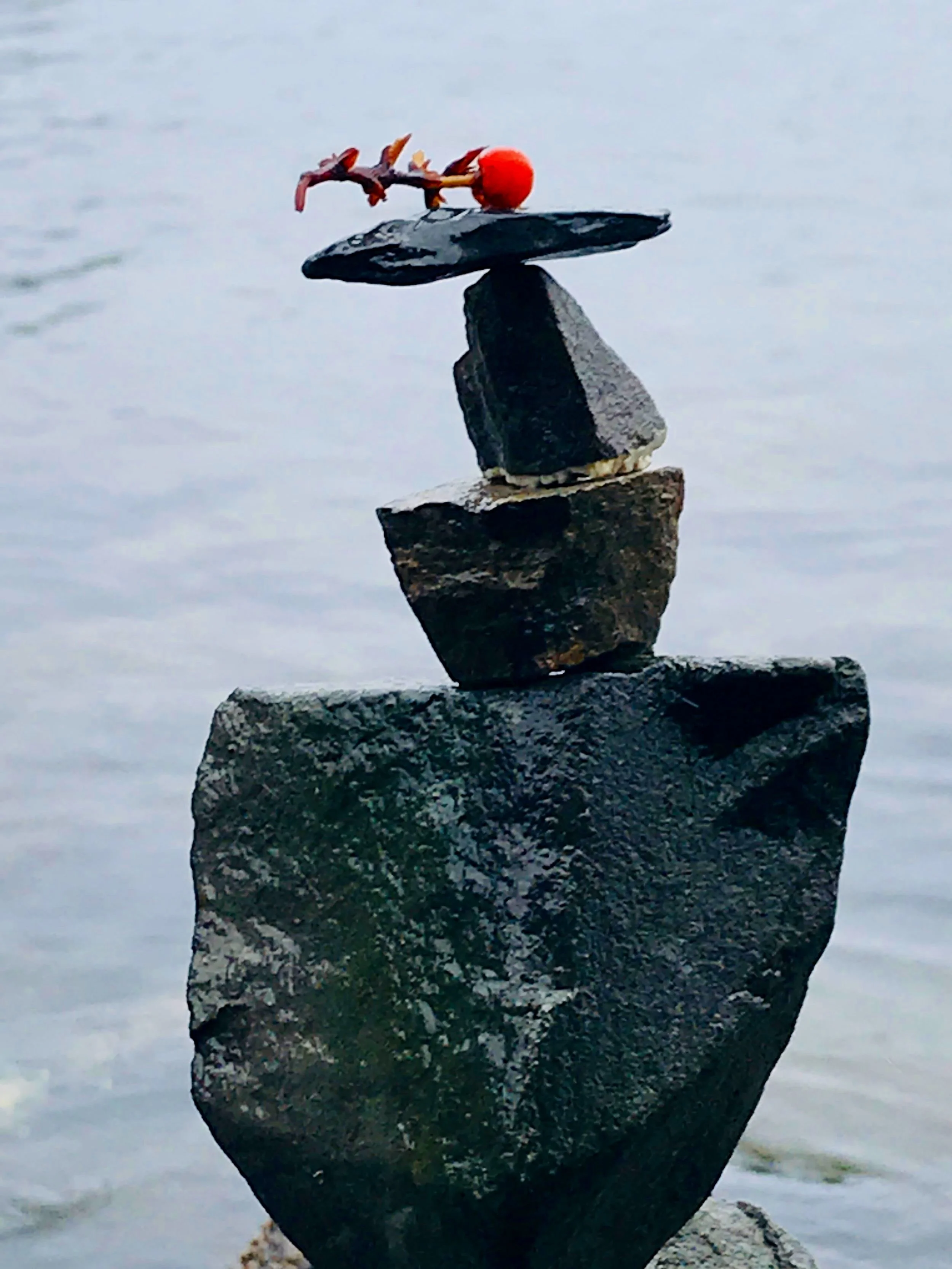 Stacked black rocks balancing on water with a small red and orange branch on top.