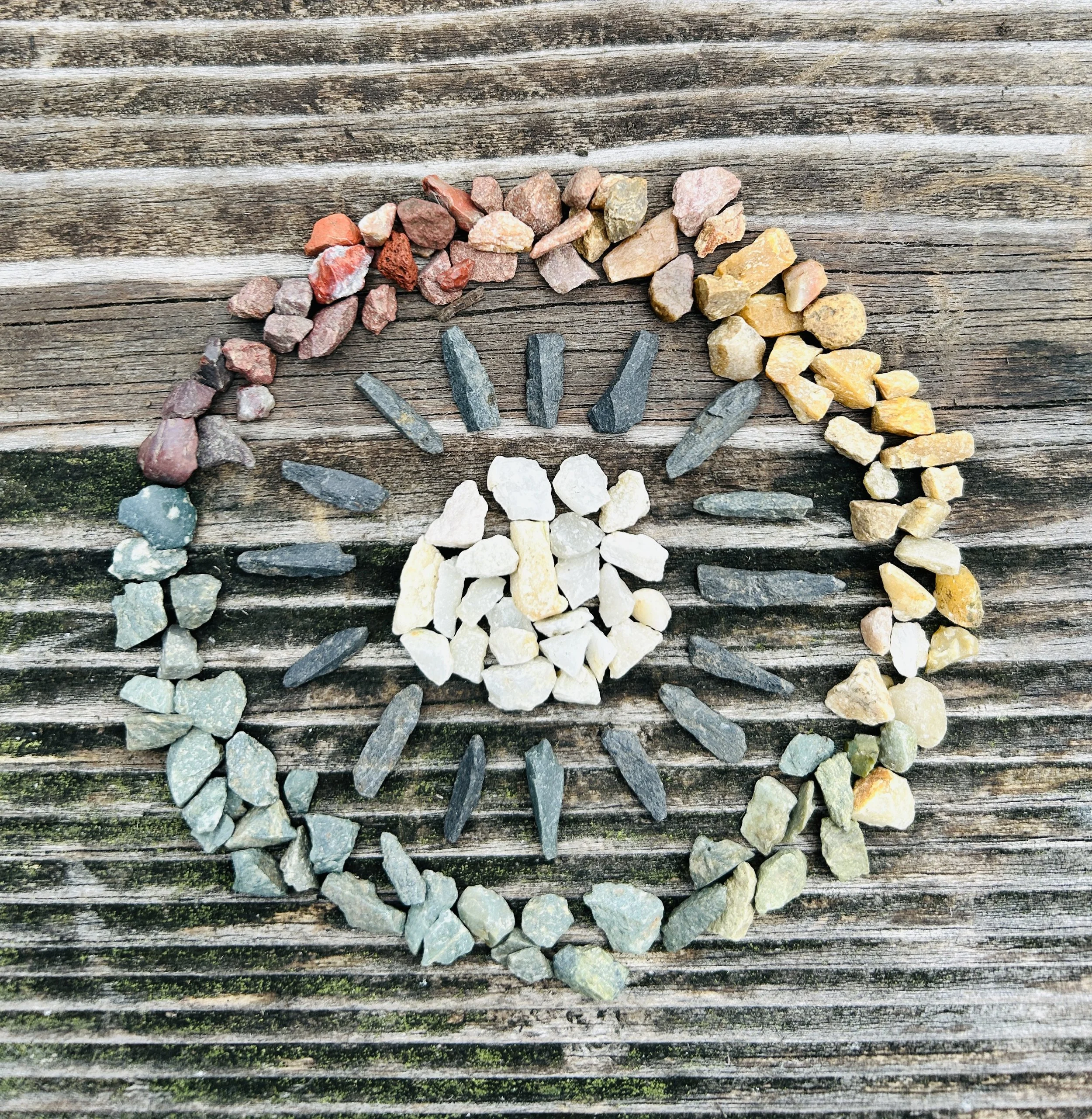 Colorful stones arranged in a rainbow mandala on a wooden surface.