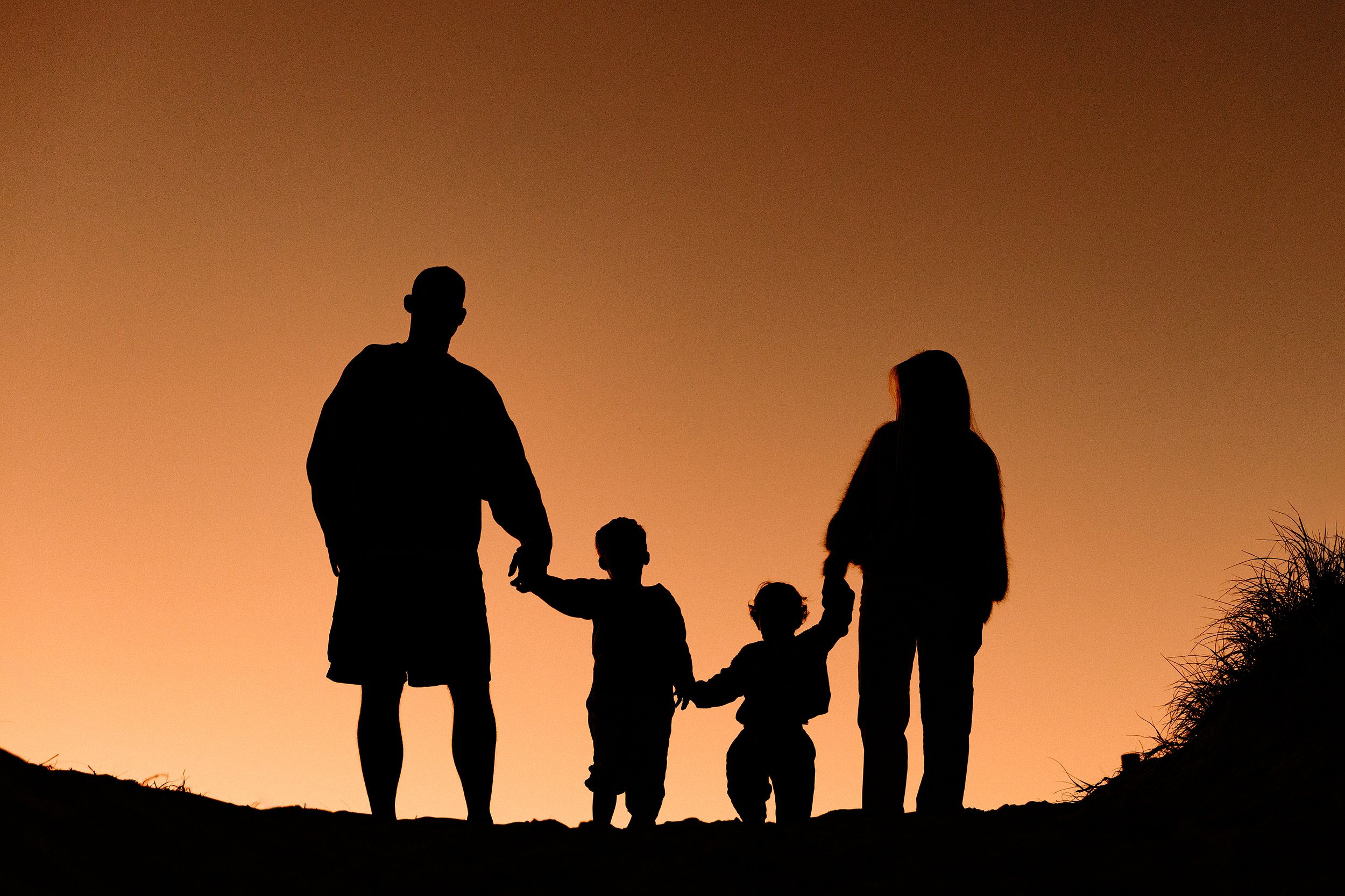 Silhouette of a family holding hands on a hill during sunset.