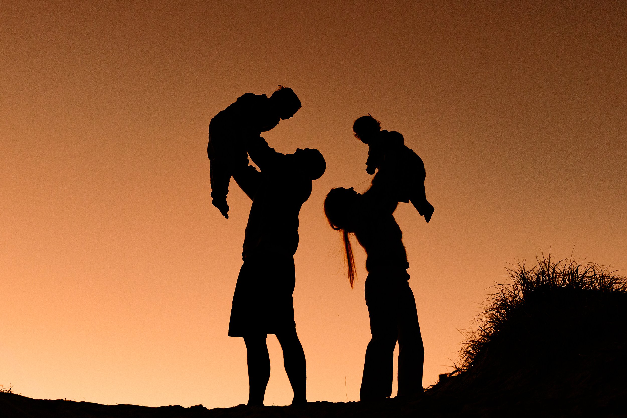 Silhouette of two adults holding children in their arms during sunset