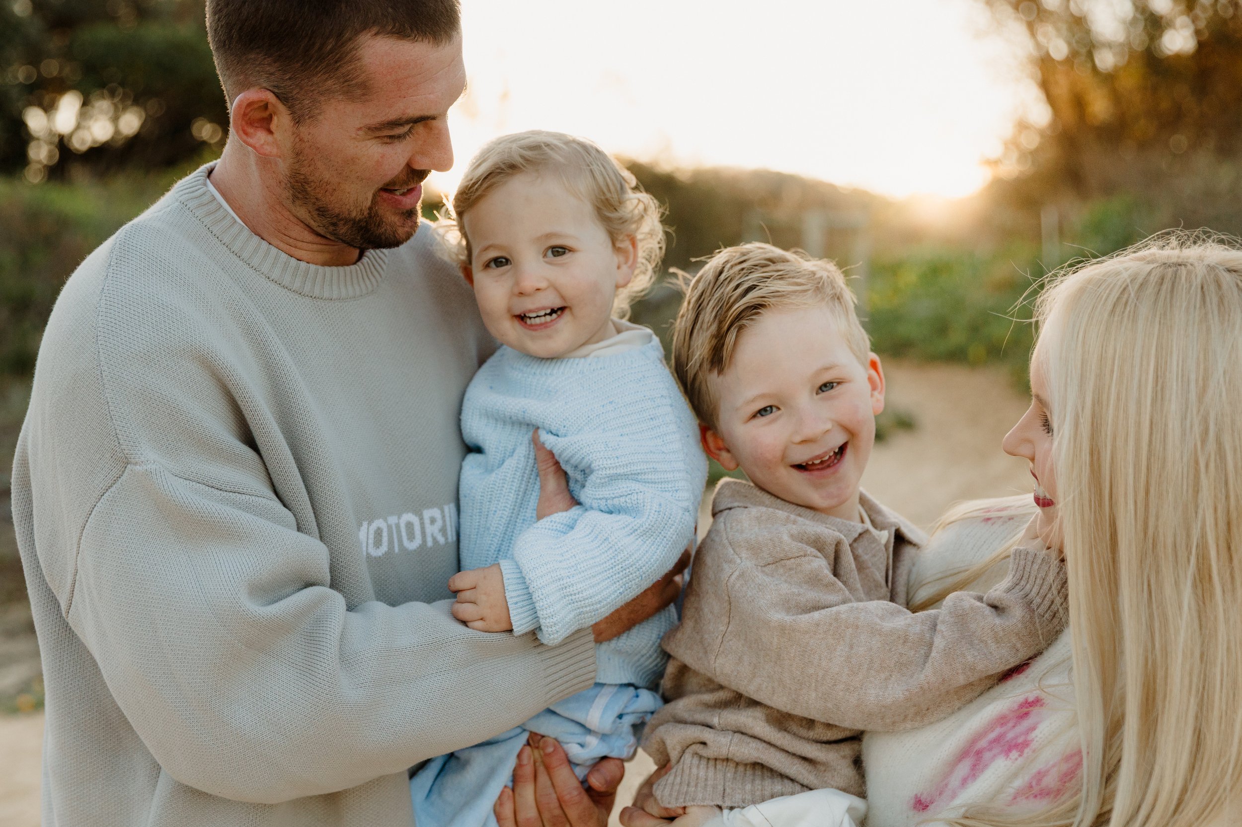 A family of four, including a man, a woman, and two young children, enjoying a moment outdoors at sunset.