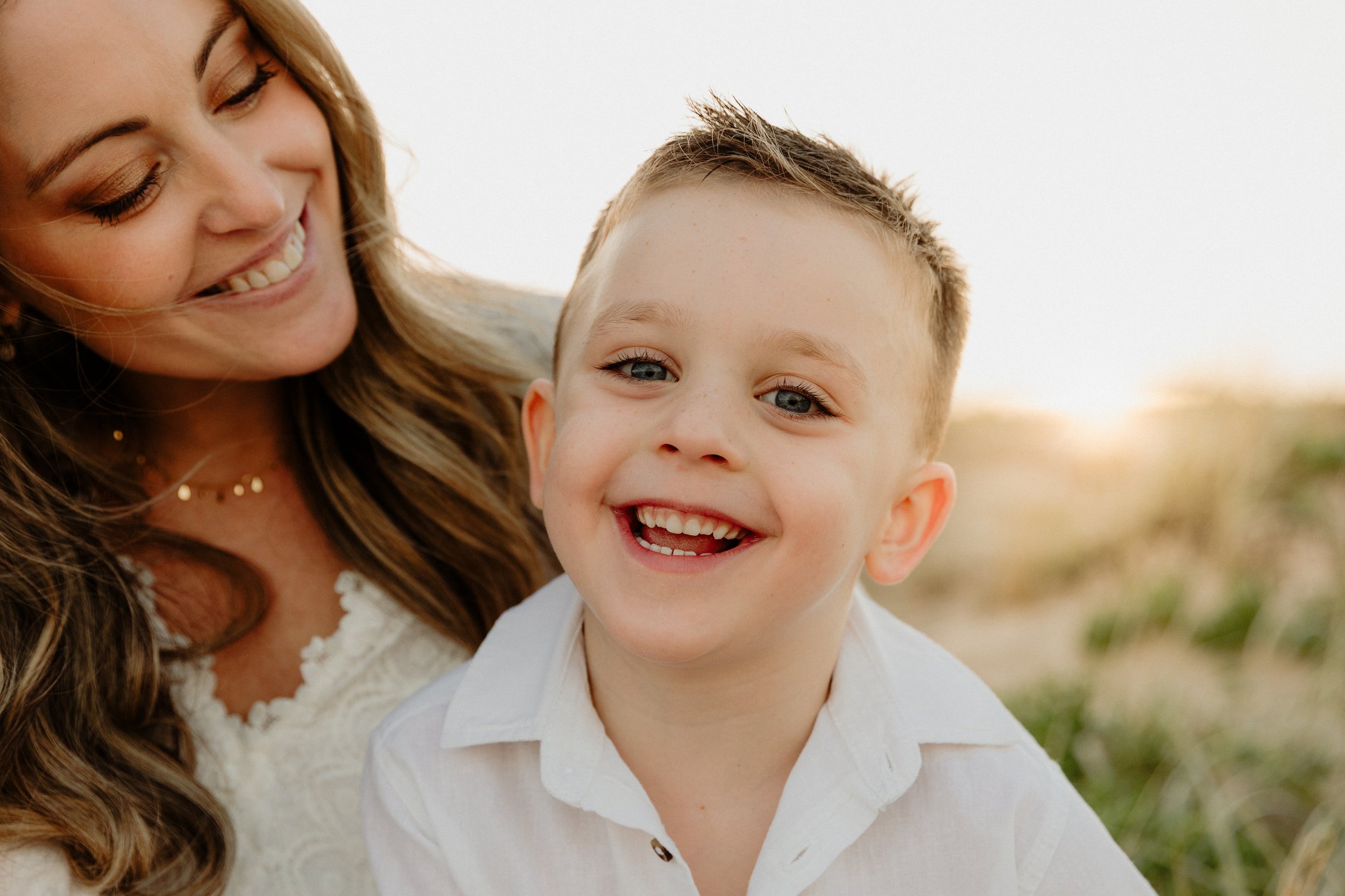 A woman and a young boy smiling happily outdoors during sunset.
