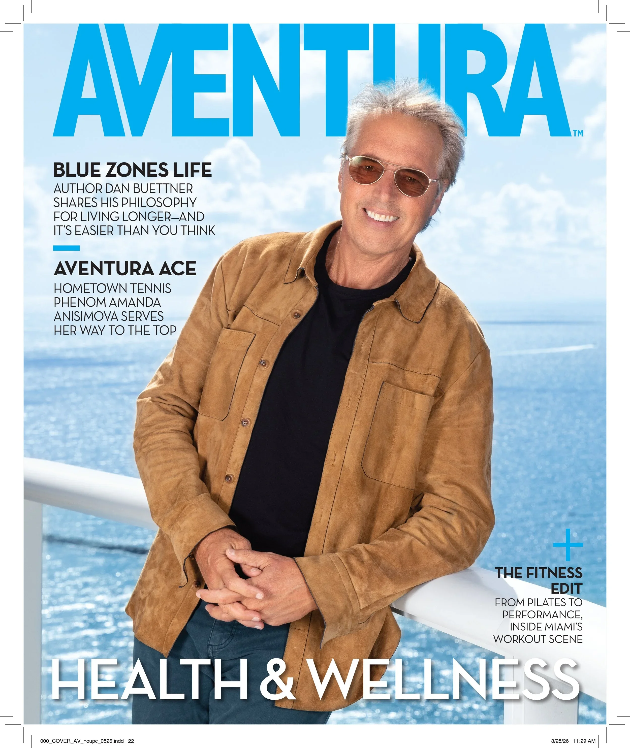 Magazine cover featuring a smiling older man with gray hair, wearing sunglasses, a black shirt, and a brown jacket, standing outdoors near a body of water under a partly cloudy sky.