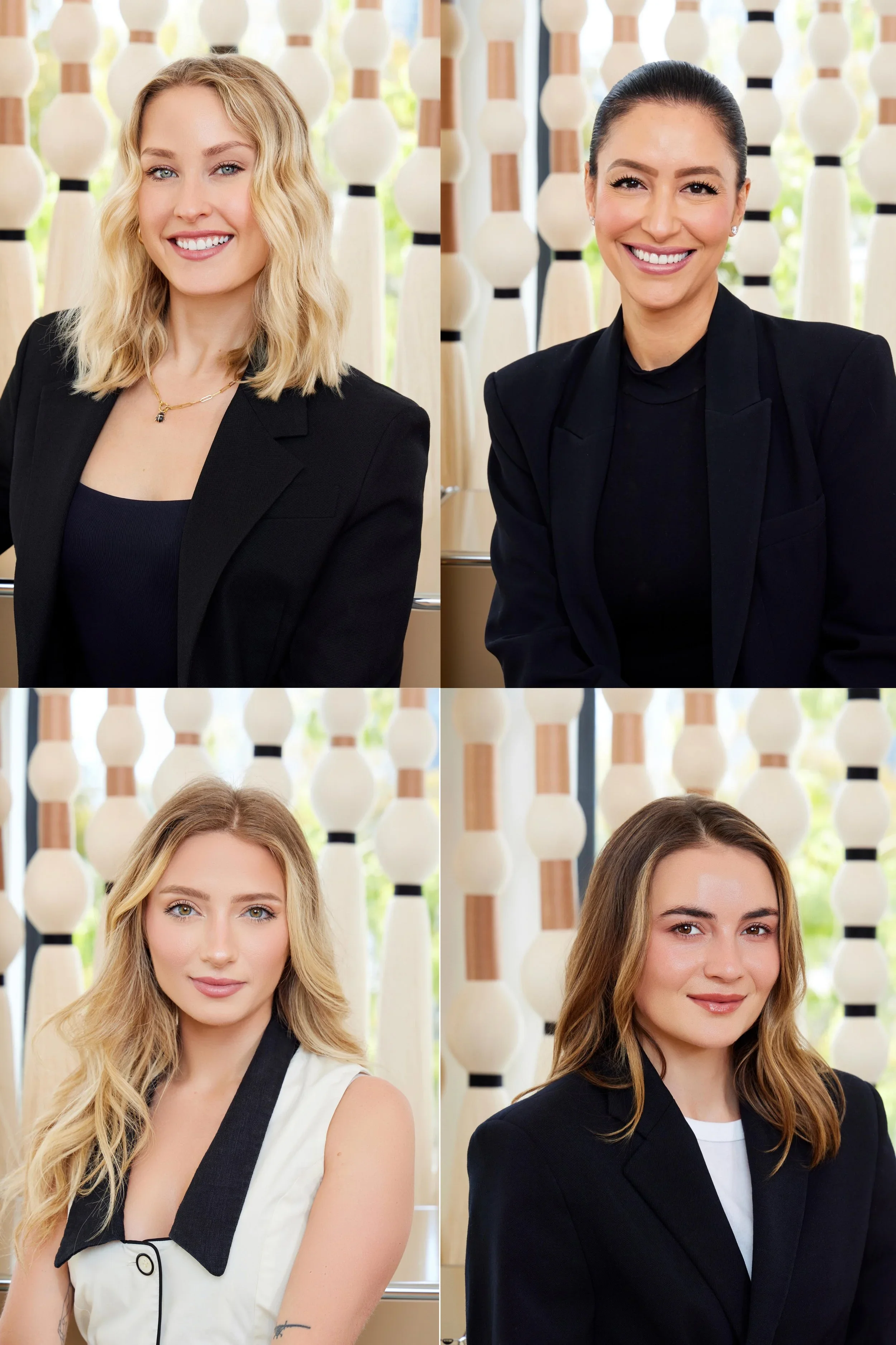 Four women with different hairstyles and makeup, wearing professional outfits, standing in front of a decorative backdrop with wooden and white elements, posing for a portrait.