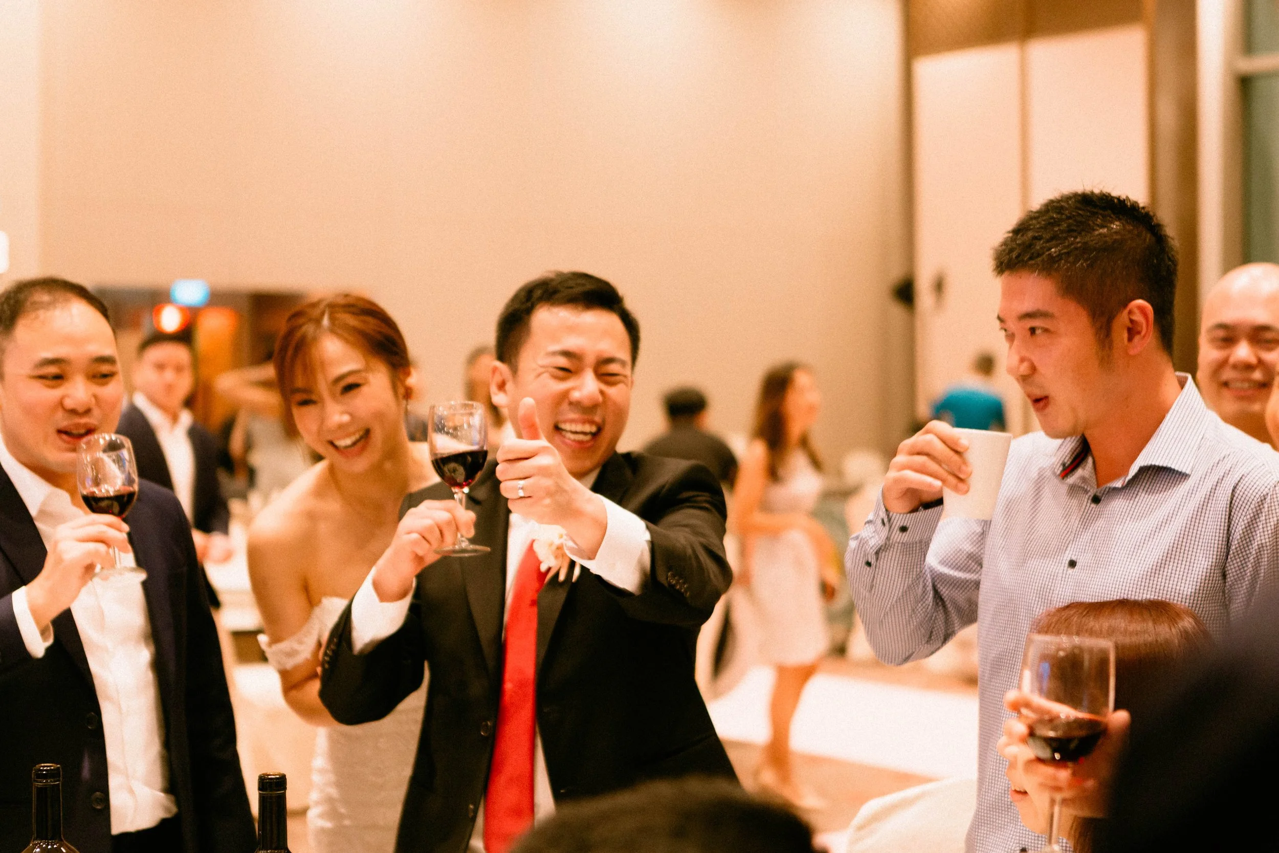 Group of people smiling, holding glasses of red wine and a coffee mug at a celebration or party.