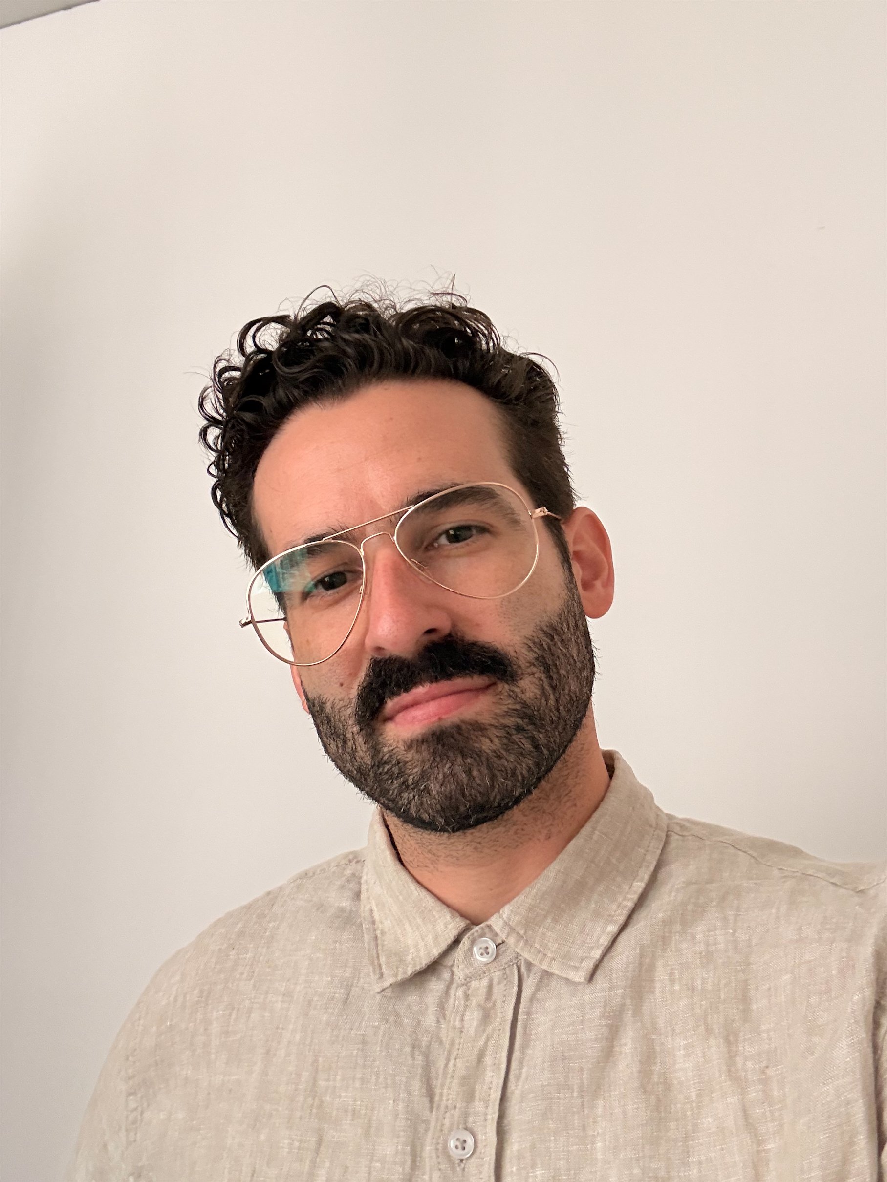 Kelvin Martinez with curly hair and beard wearing a suit and tie in front of red flowers