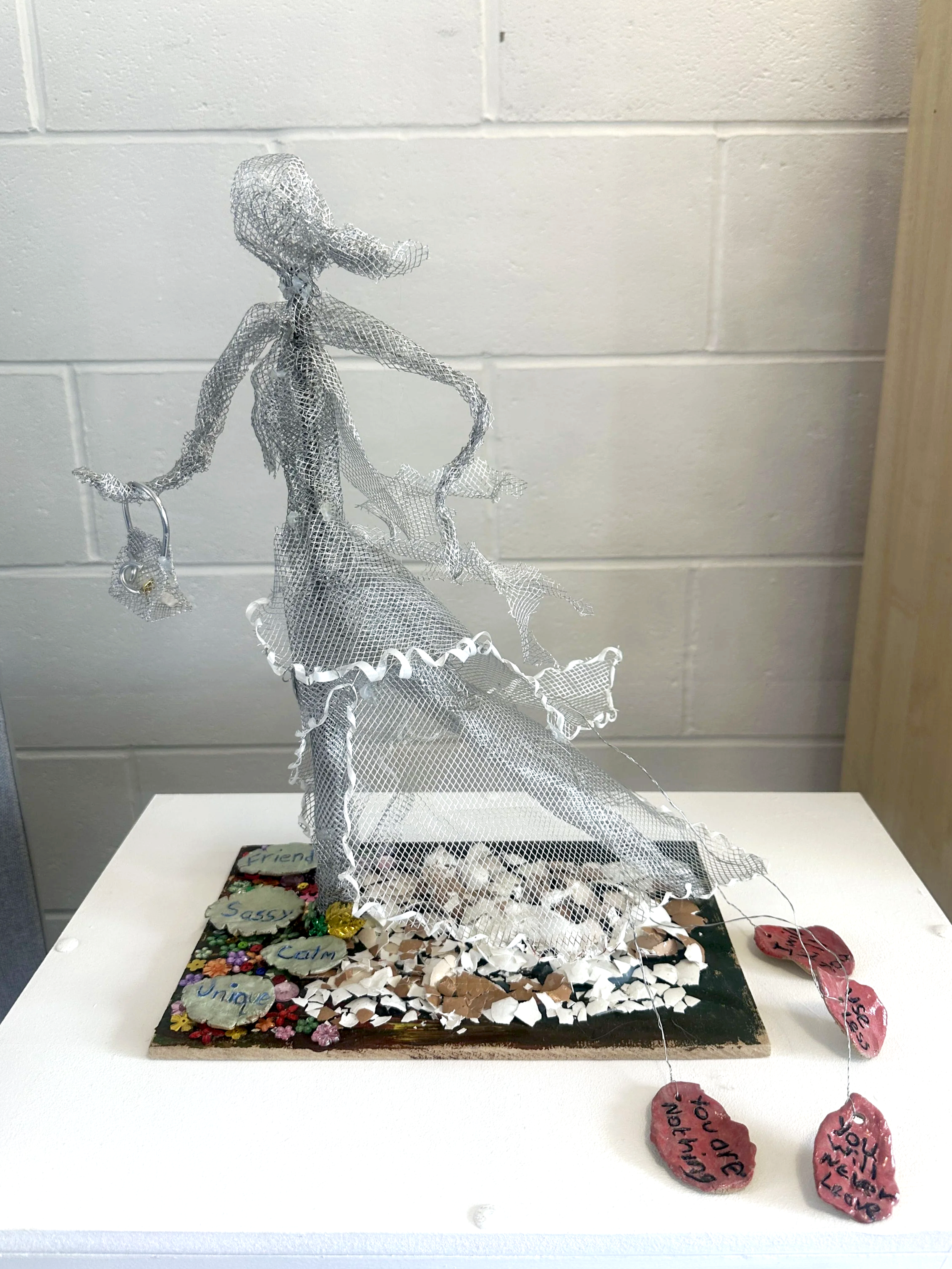 Sculpture made of wire-mesh of a woman wearing a dress. Clay petals are falling from the back of her dress.