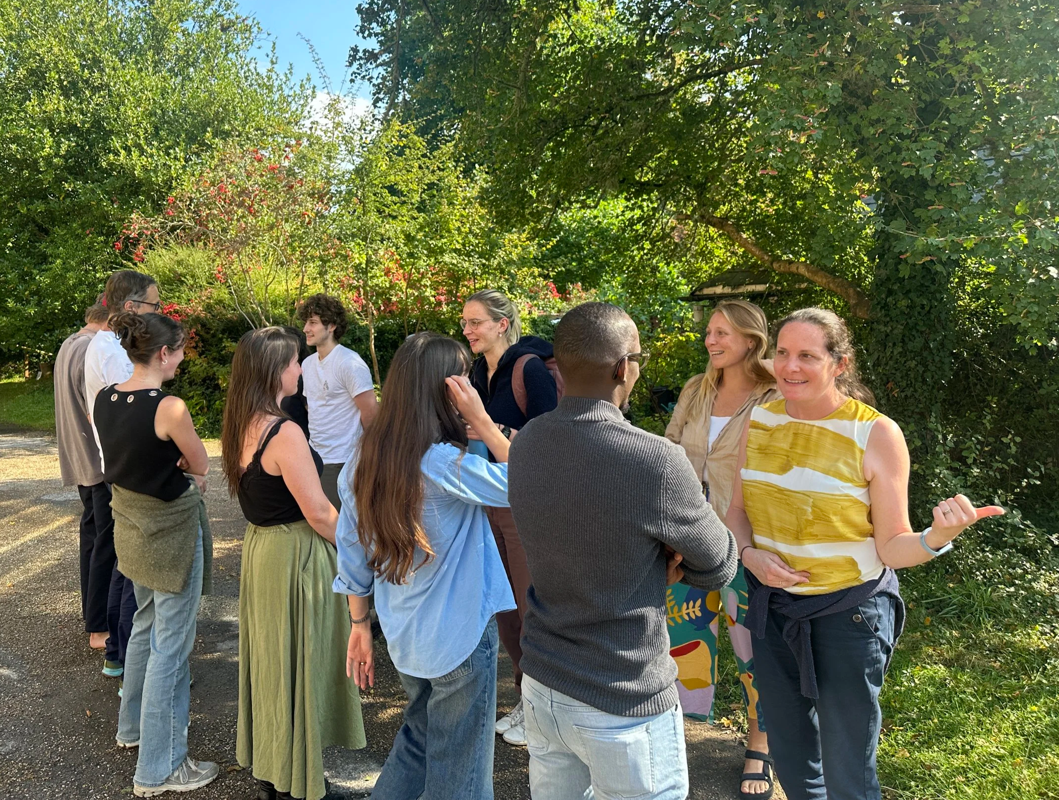 Group of people doing a facilitated feedback session outdoors in a garden with trees and bushes.