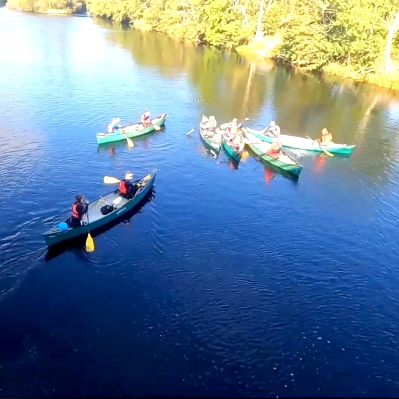 Young people in 6 canoes on the River Spey. The water is flat and the weather is sunny.