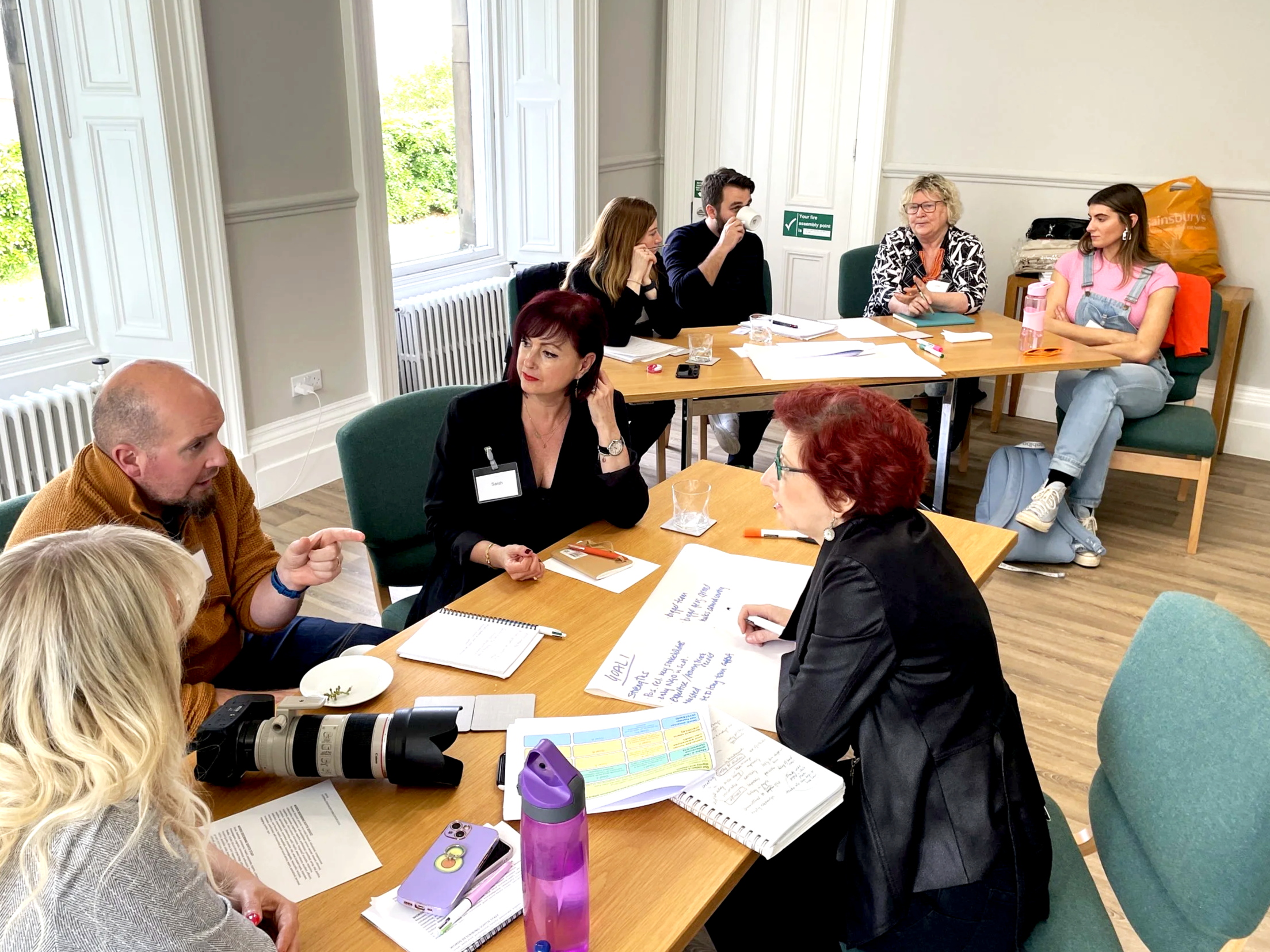 Staff Team and Board Members from SOHTIS taking part in a strategy session. They are in groups of 4-5 sitting around two tables.