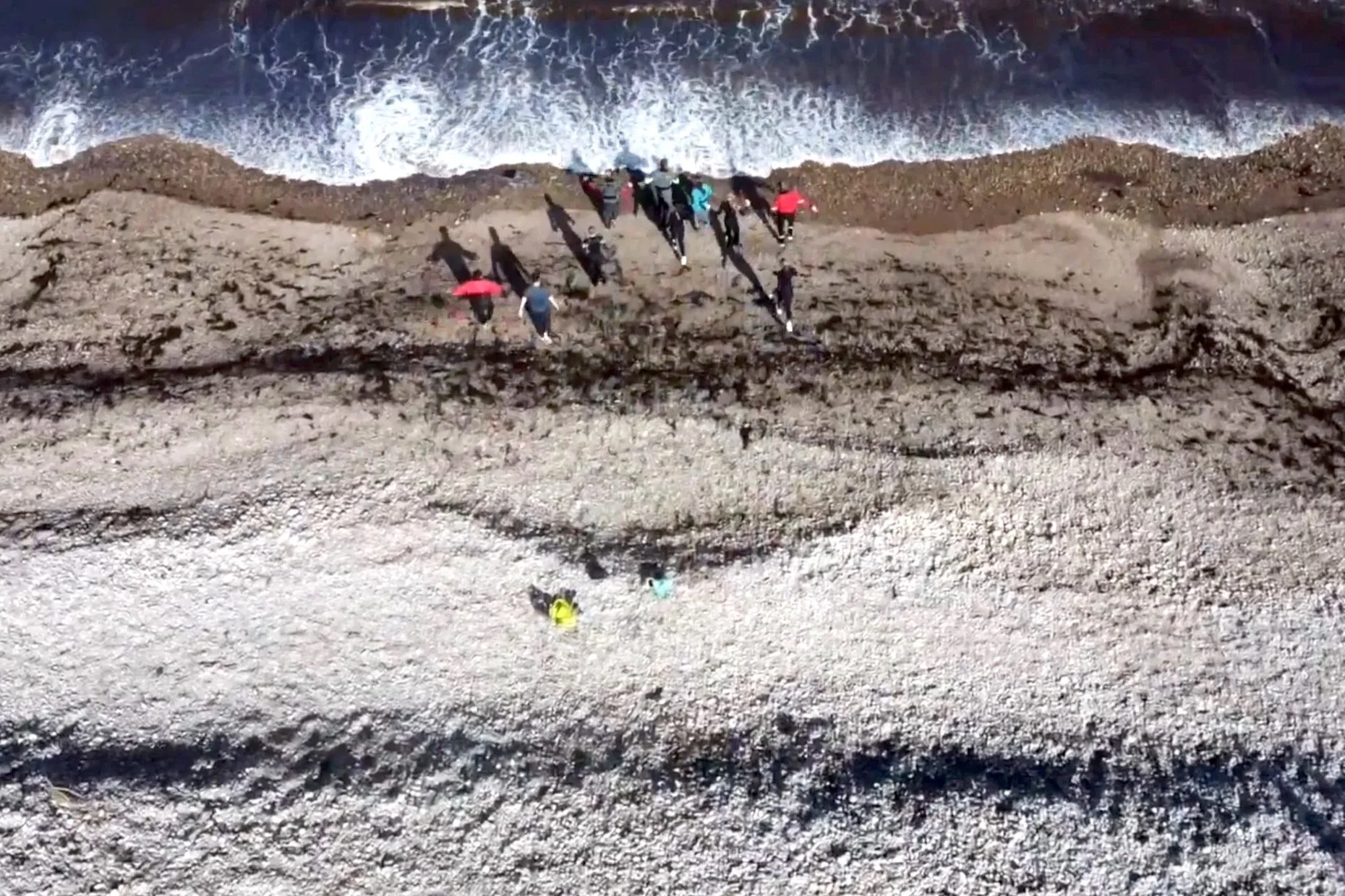 Aerial shot of young people walking into the sea at the end of a canoe expedition down the River Spey in Scotland.