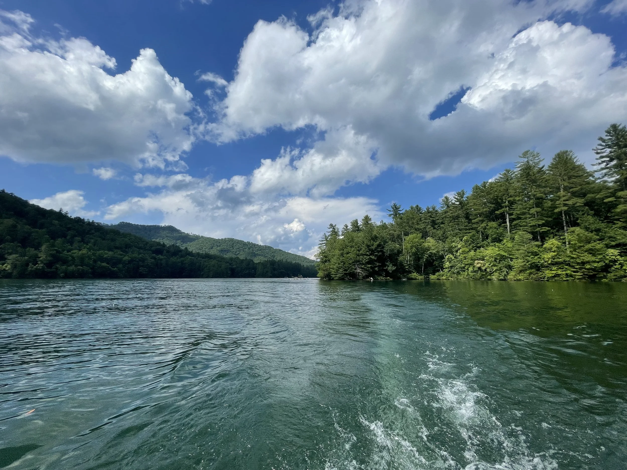 A scenic view of a lake with trees on both sides under a partly cloudy sky.
