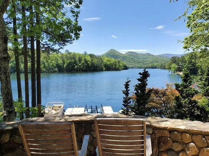 A peaceful lake surrounded by dense forest under a sky with scattered clouds during sunset.