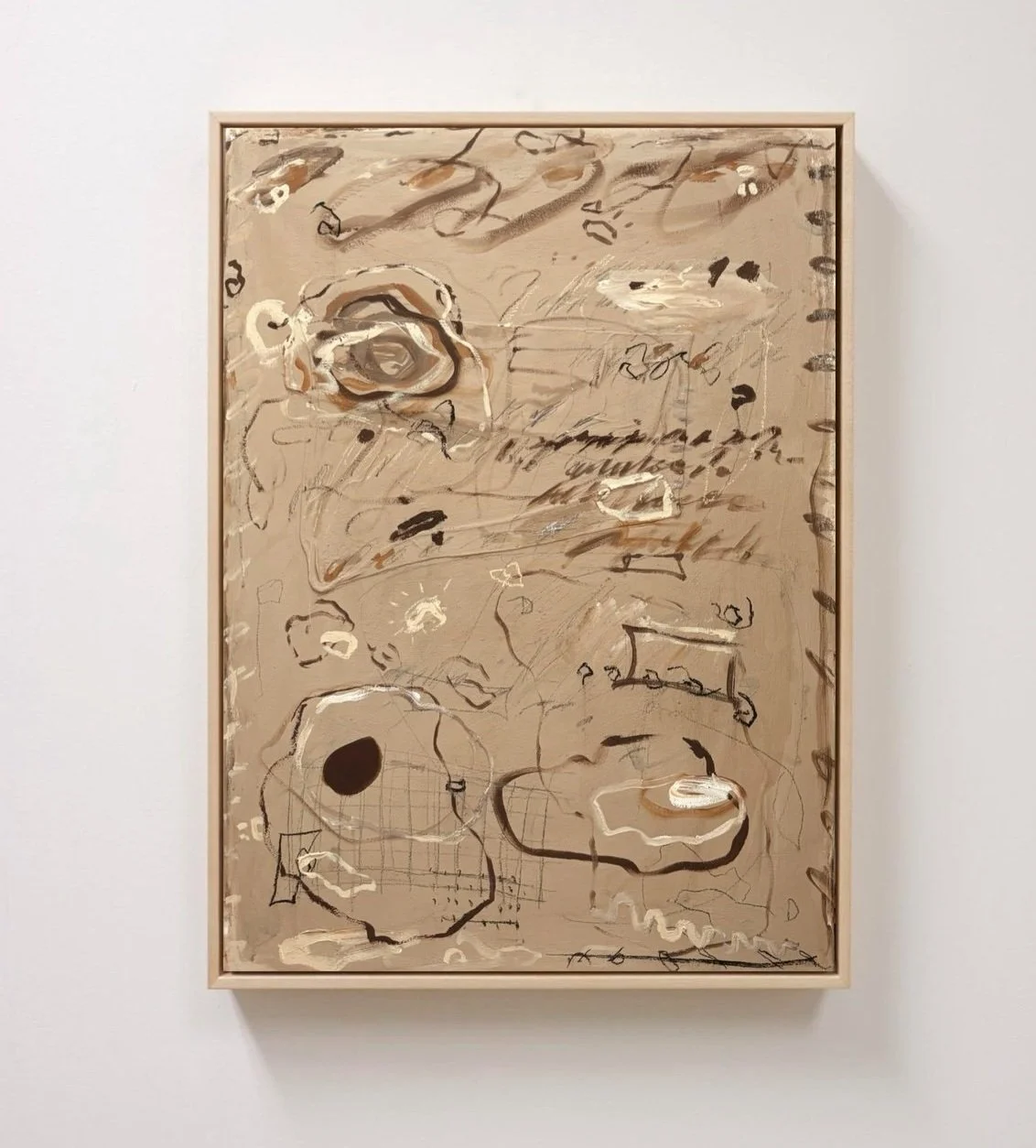 Abstract painting with scribbles, shapes, and colors on a beige background, framed on a white wall.