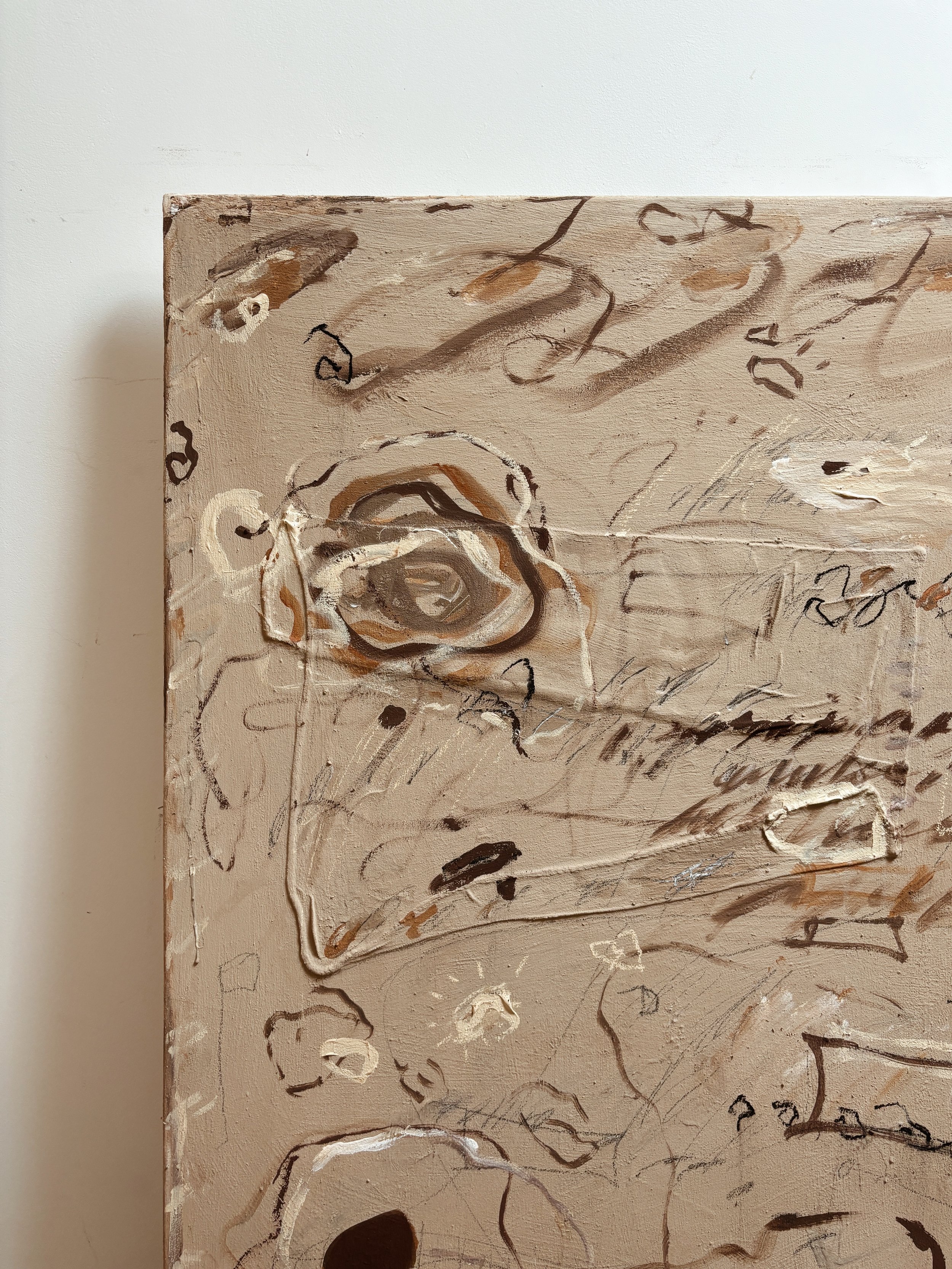 Close-up of an abstract painting with beige, brown, black, and white brush strokes and scribbles on a piece of canvas.