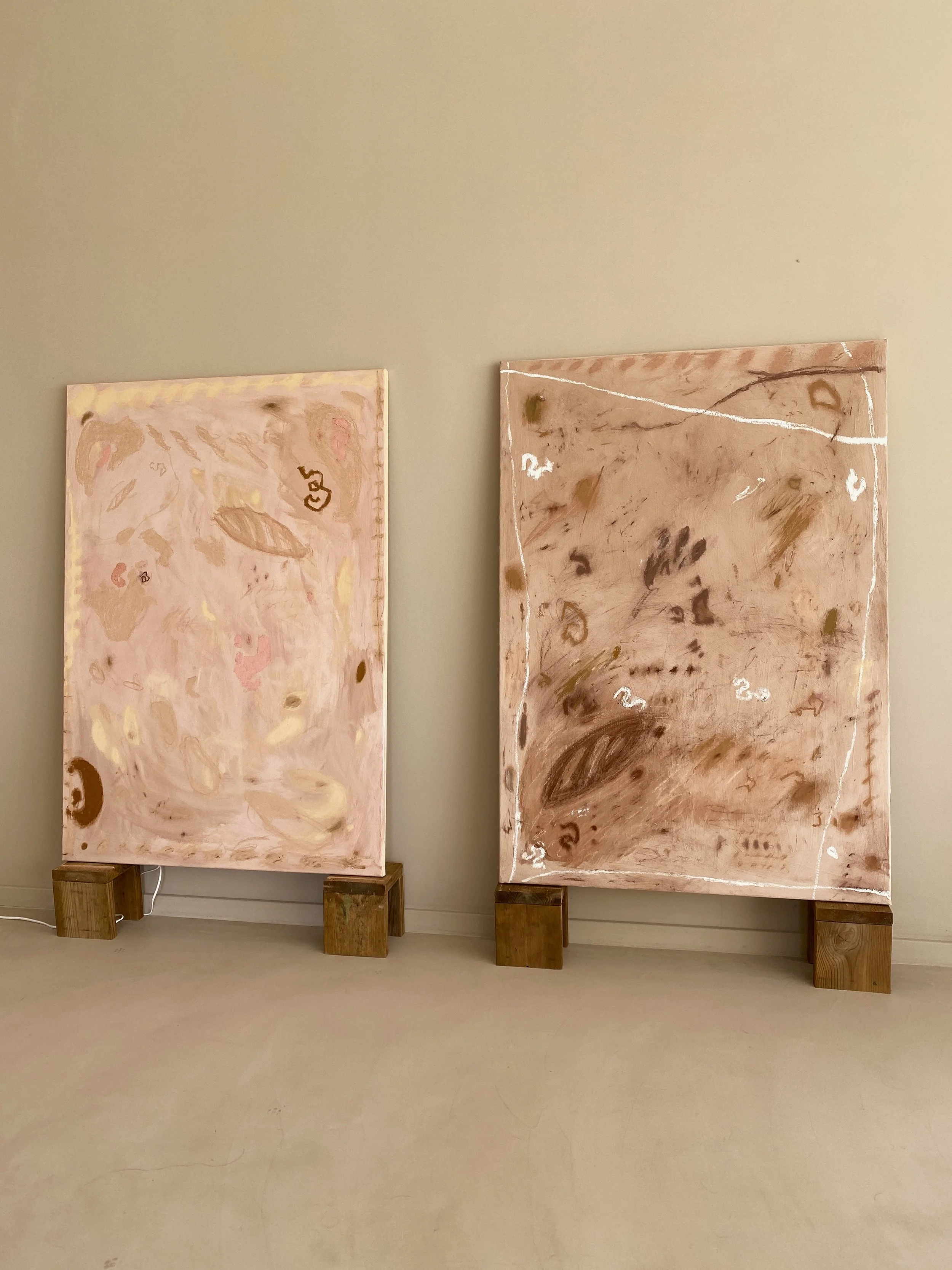 Two abstract paintings with organic swirling patterns in light pink, brown, and beige, mounted on wooden blocks against a plain wall.