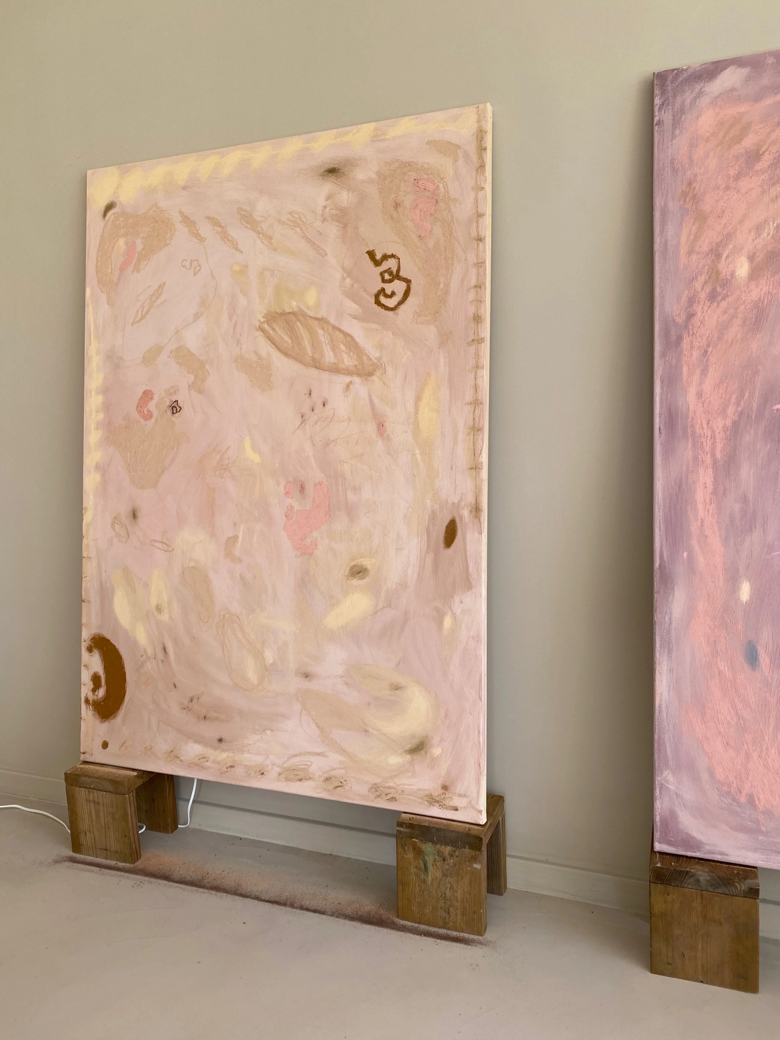 Abstract painting with soft pink, beige, and light brown tones, mounted on a cardboard stand with wooden blocks at the bottom.