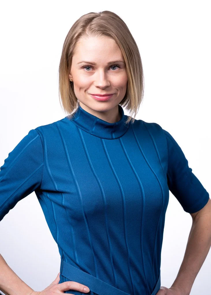 Nainen sinisessä poolopaidassa kädet lantiolla, valkoinen tausta