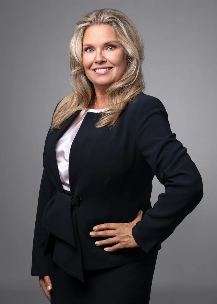 Vaaleahiuksinen nainen mustassa jakussa ja valkoisessa paidassa hymyilee