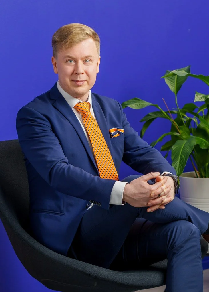 LeadDeskin työntekijä sinisessä puvussa ja oranssissa solmiossa nojatuolissa