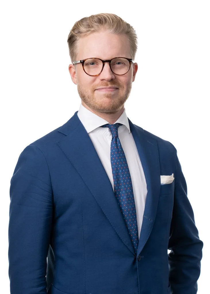 Silmälasipäinen mies sinisessä puvussa ja pilkullisessa solmiossa