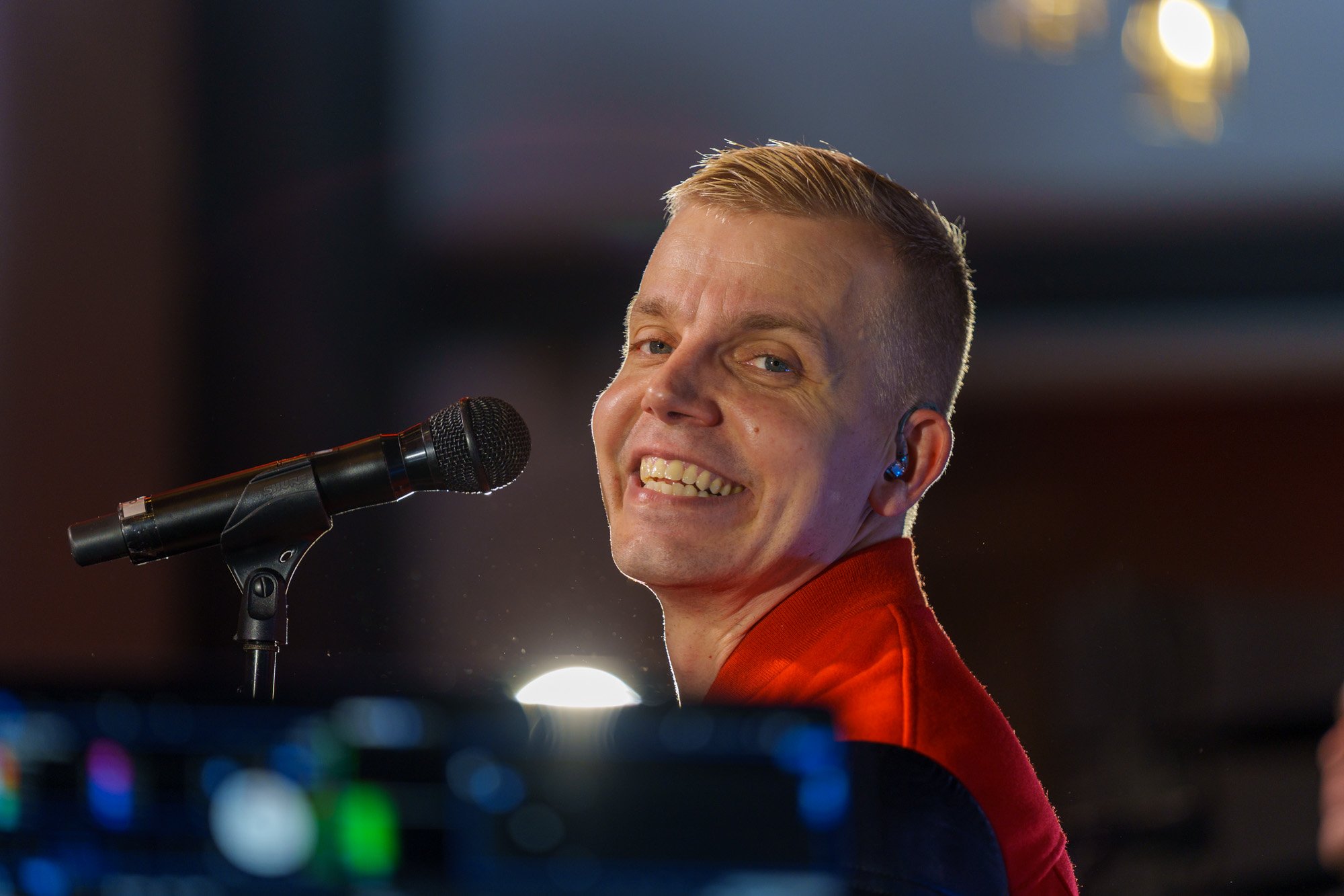 Hymyilevä mies puhuu mikrofonilla, taustalla kaupungin valoja illalla.