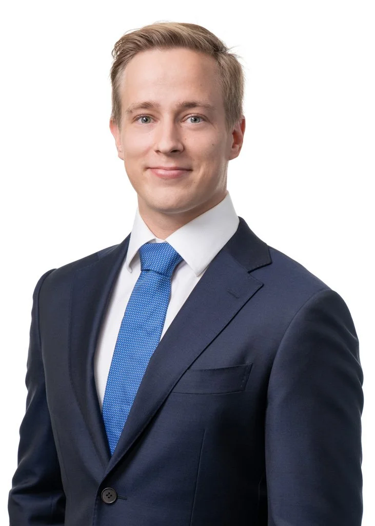 Nuori mies tummansinisessä puvussa ja sinisessä solmiossa, valkoinen tausta