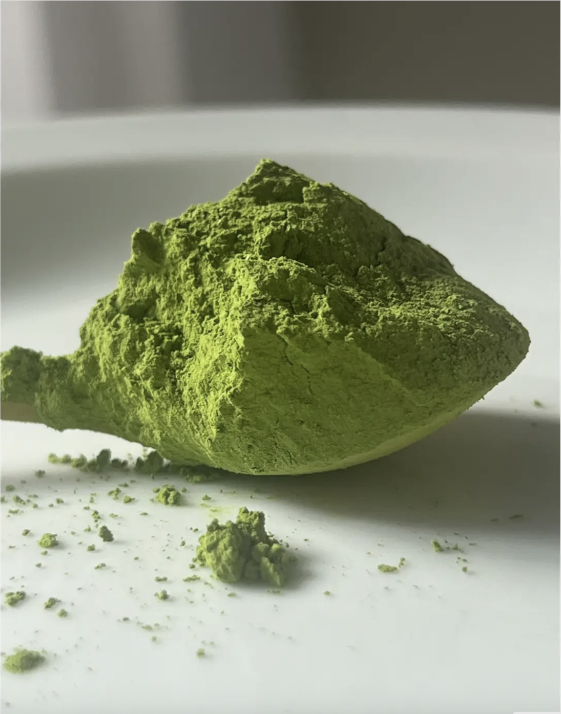 Close-up of a mound of bright green matcha powder on a white surface.