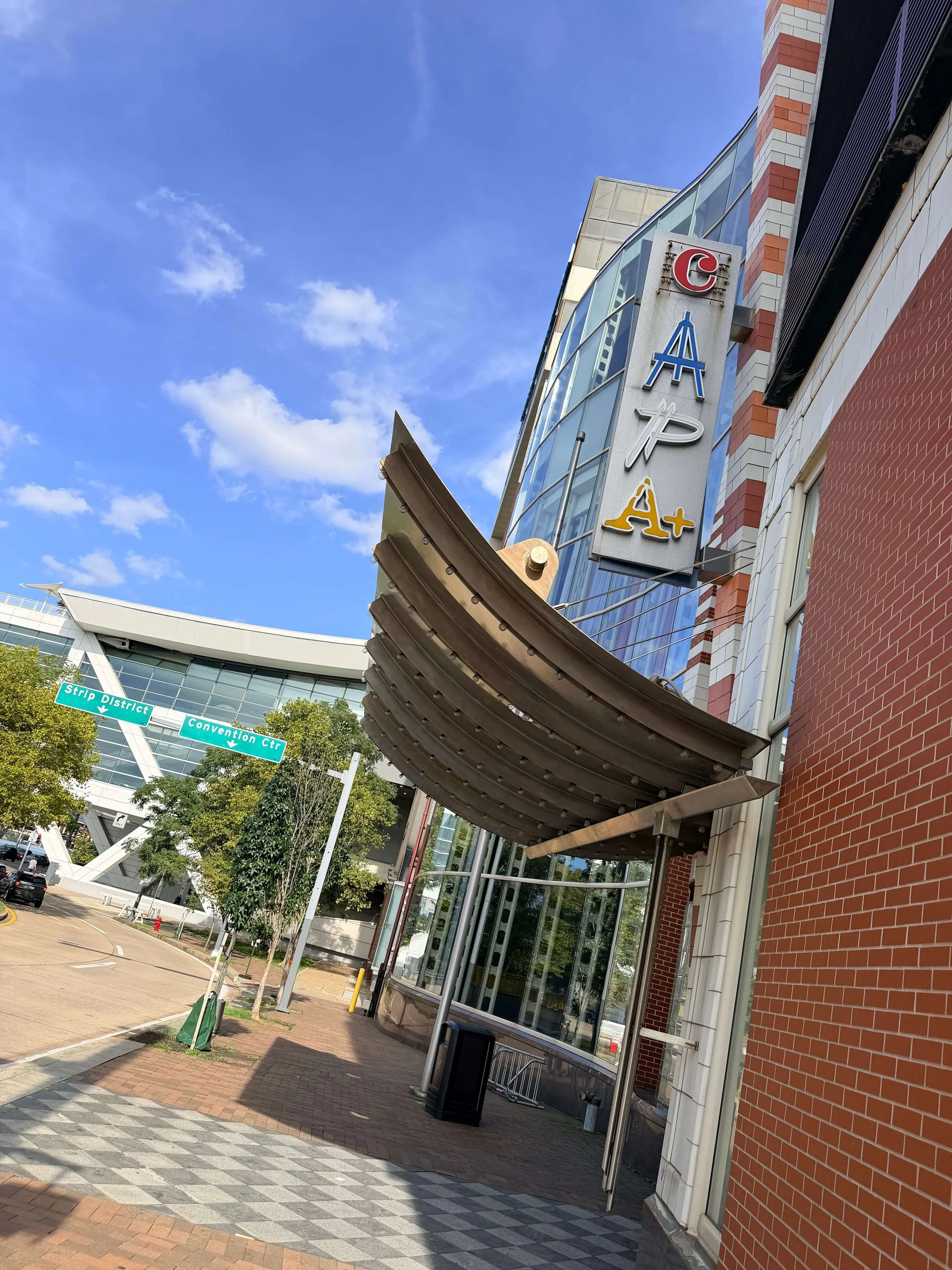 Downtown streetscape with a vertical “C H A P E L” sign, Convention Center and Strip District directional signs, brick buildings, and a blue sky.