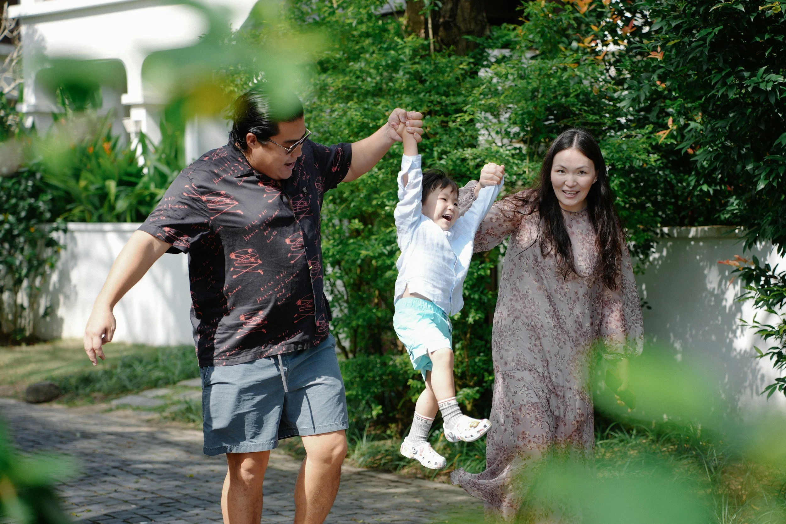 pod health, parents playing with child, smiling and swinging in the air.