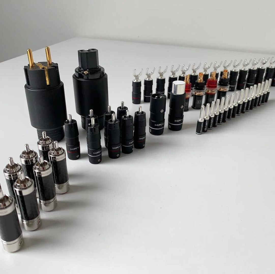 Arrangement of various audio equipment connectors, including RCA connectors, power plugs, and banana plugs, on a white surface.