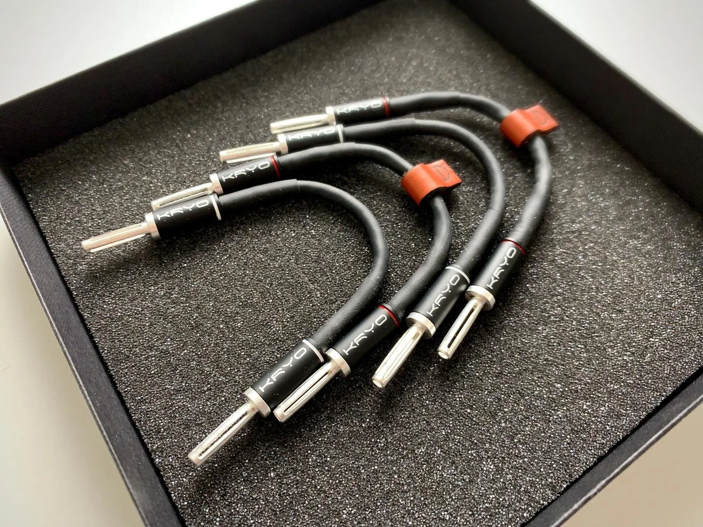 Four black audio or speaker cables with metal connectors, placed in a foam-lined black box.