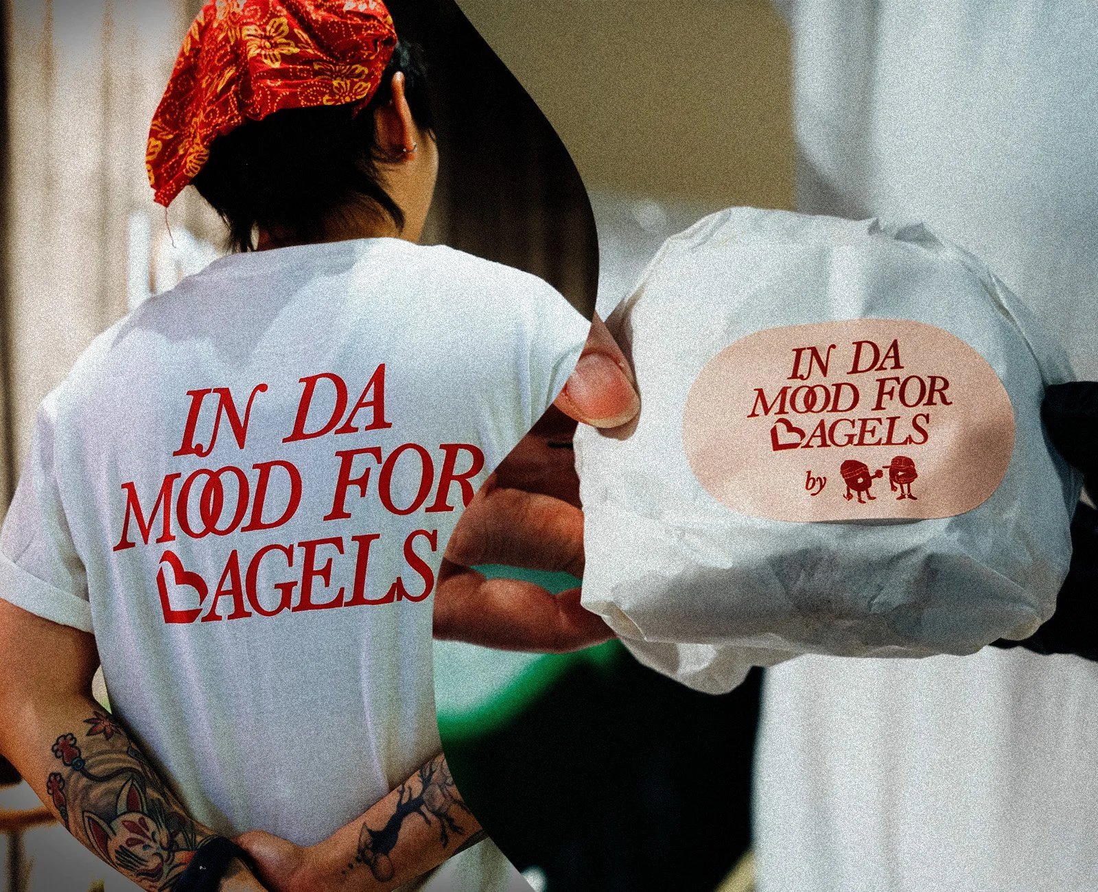 A woman with tattoos wearing a white t-shirt and a red bandana holds a wrapped burger, both with a label reading 'IN DA MOOD FOR BAGELS' and a small illustration of two bagels with legs.