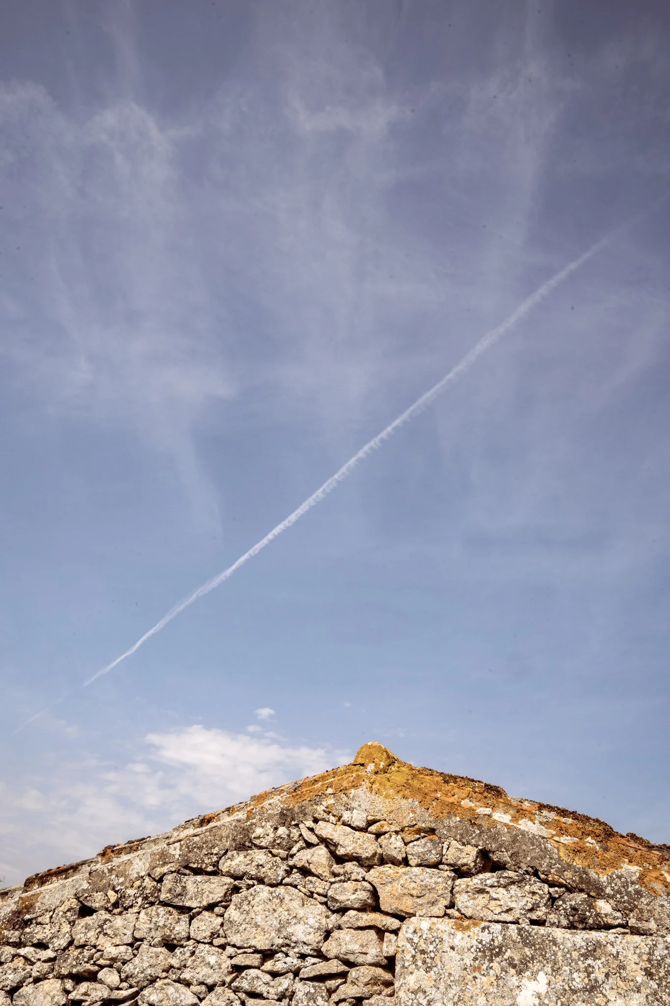 Une structure en pierre avec un ciel bleu en arrière-plan, une couche de nuages et la trace d'un avion.