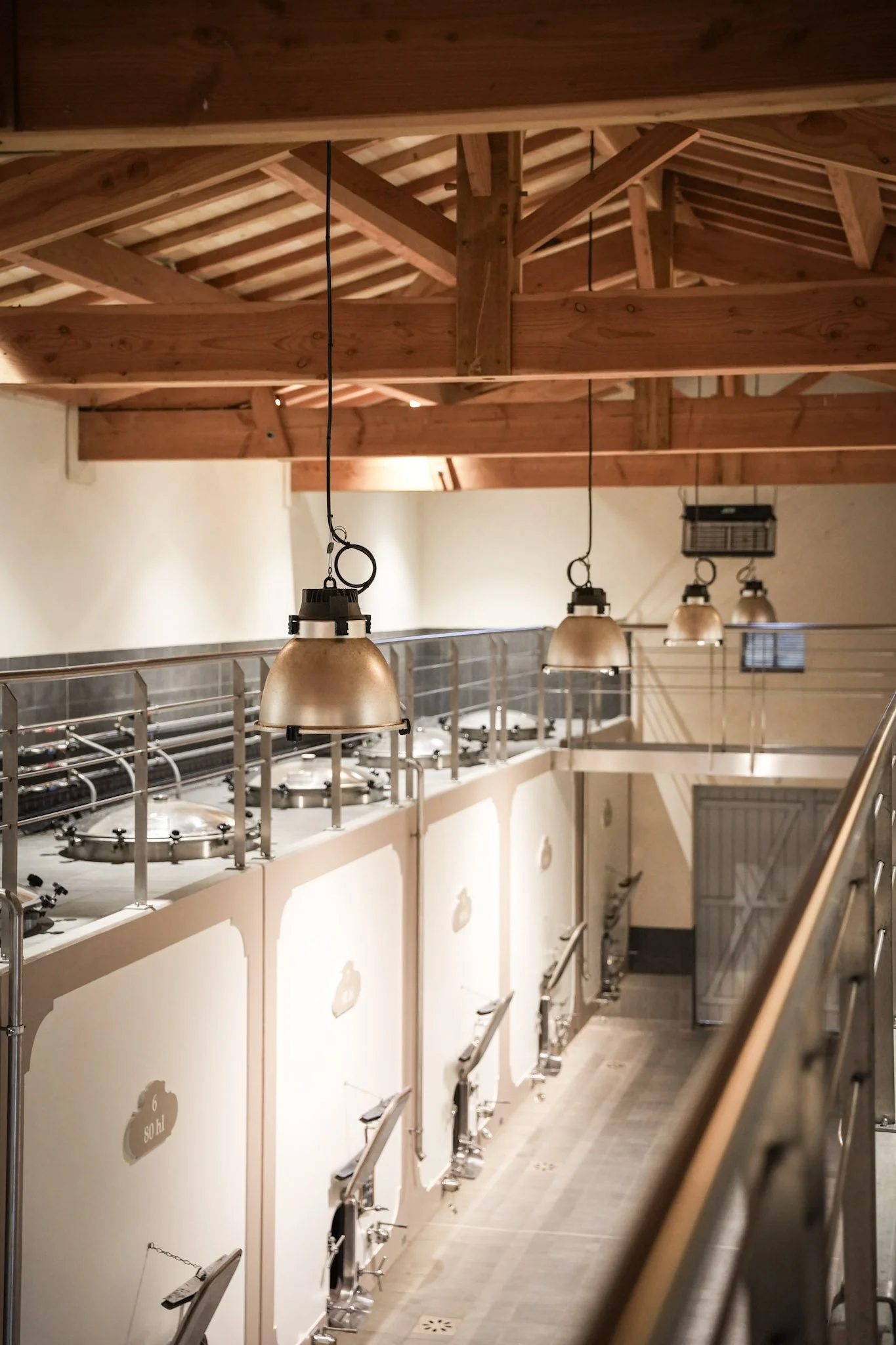 Vue intérieure d'une brasserie avec des cuves de fermentation et des lampes suspendues en cuivre, plafond en bois apparent.