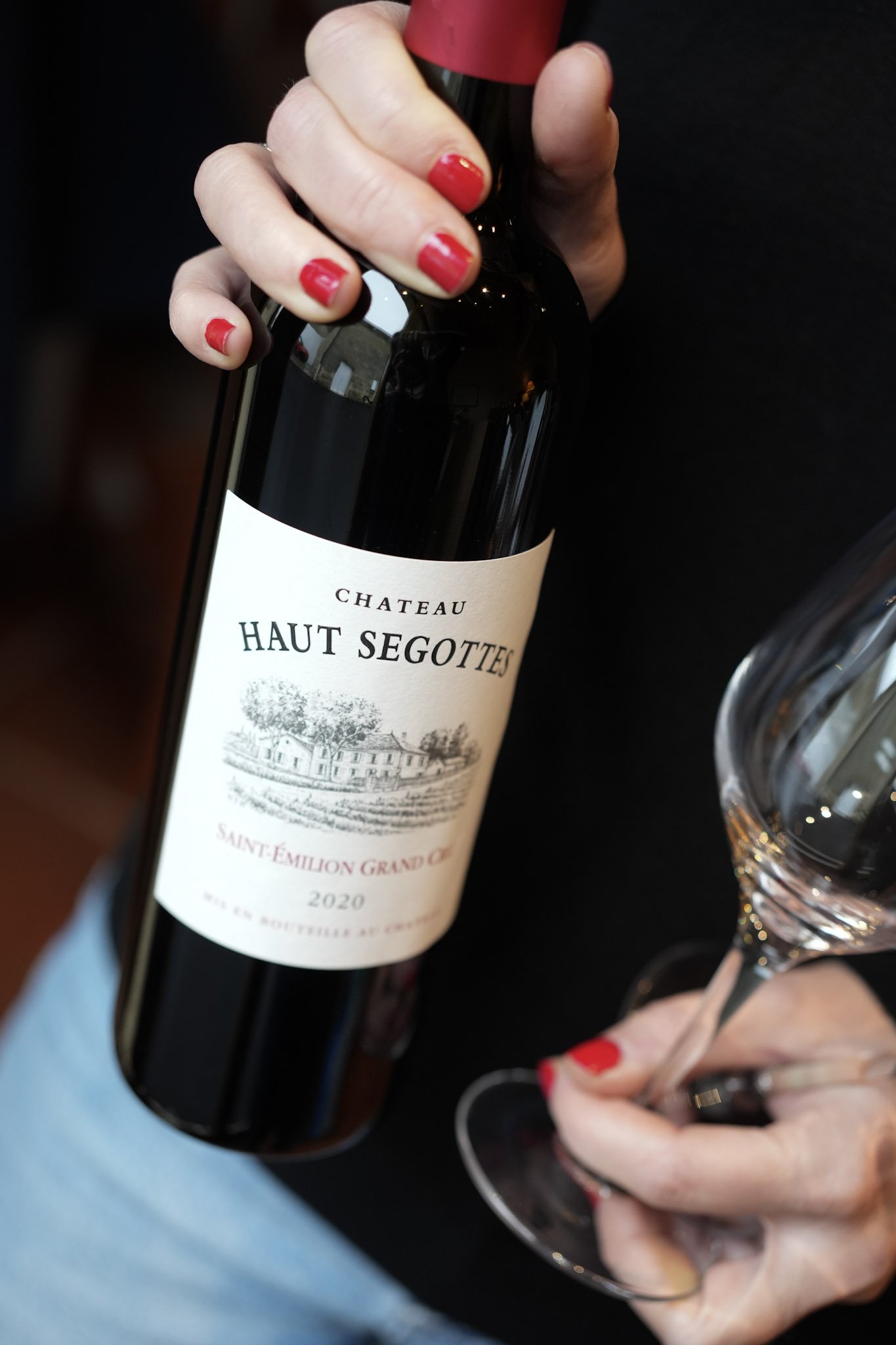 Une femme tenant une bouteille de vin rouge Château Haut Segottes 2020 et un verre à vin vide.