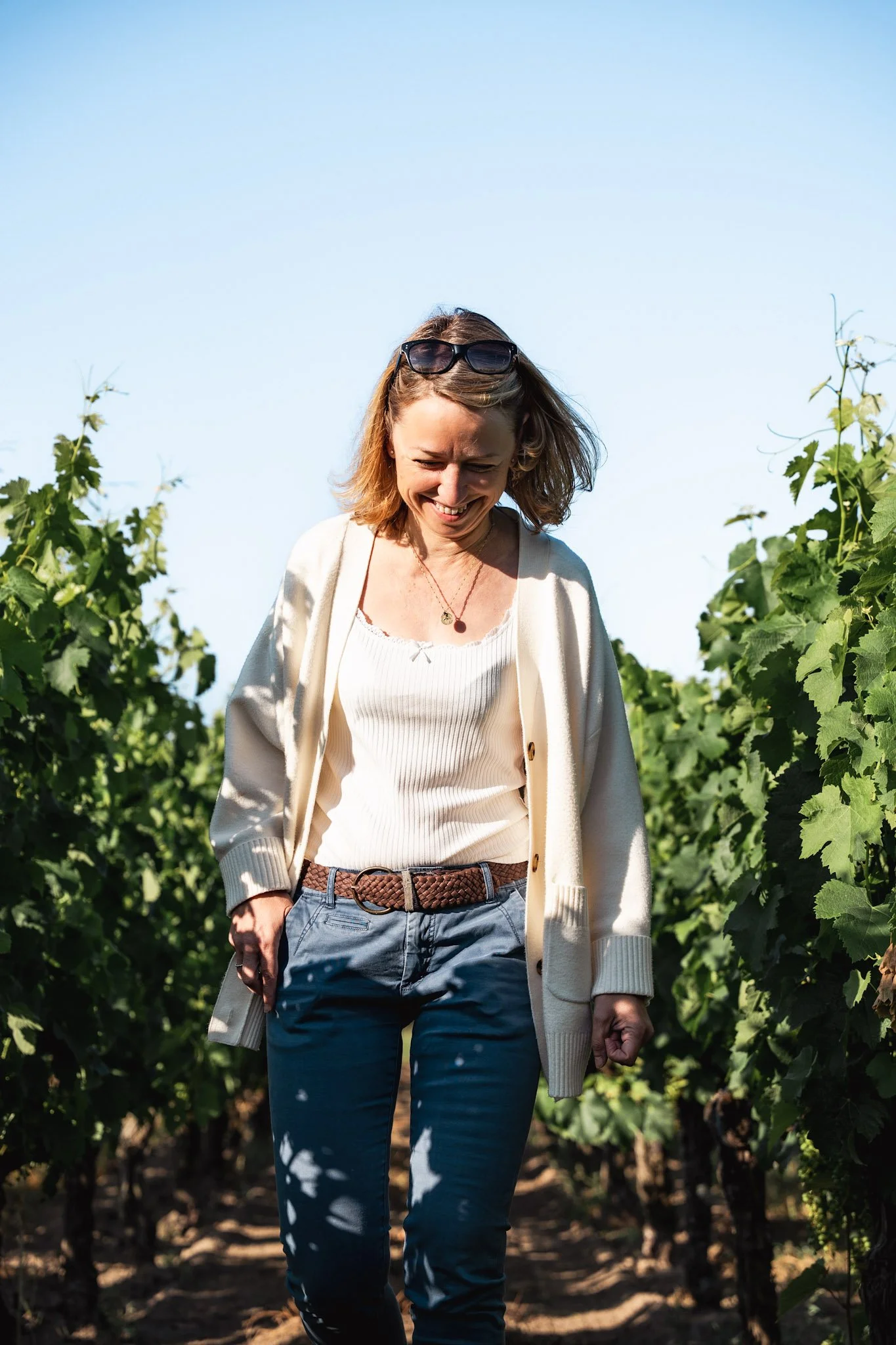 Une femme souriante dans un vignoble sous un ciel bleu clair.
