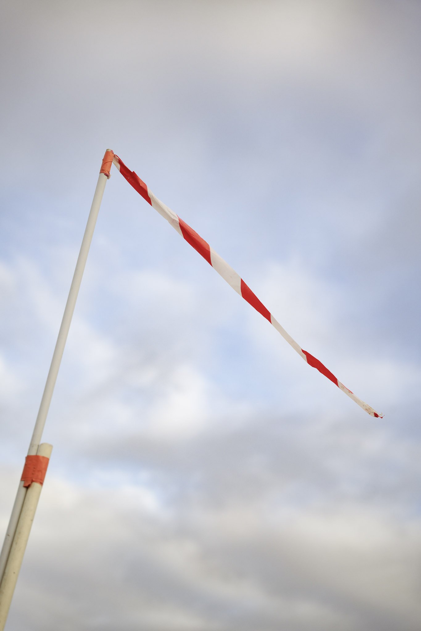 Drapeau de chantier rouge et blanc flottant dans le vent contre un ciel nuageux.