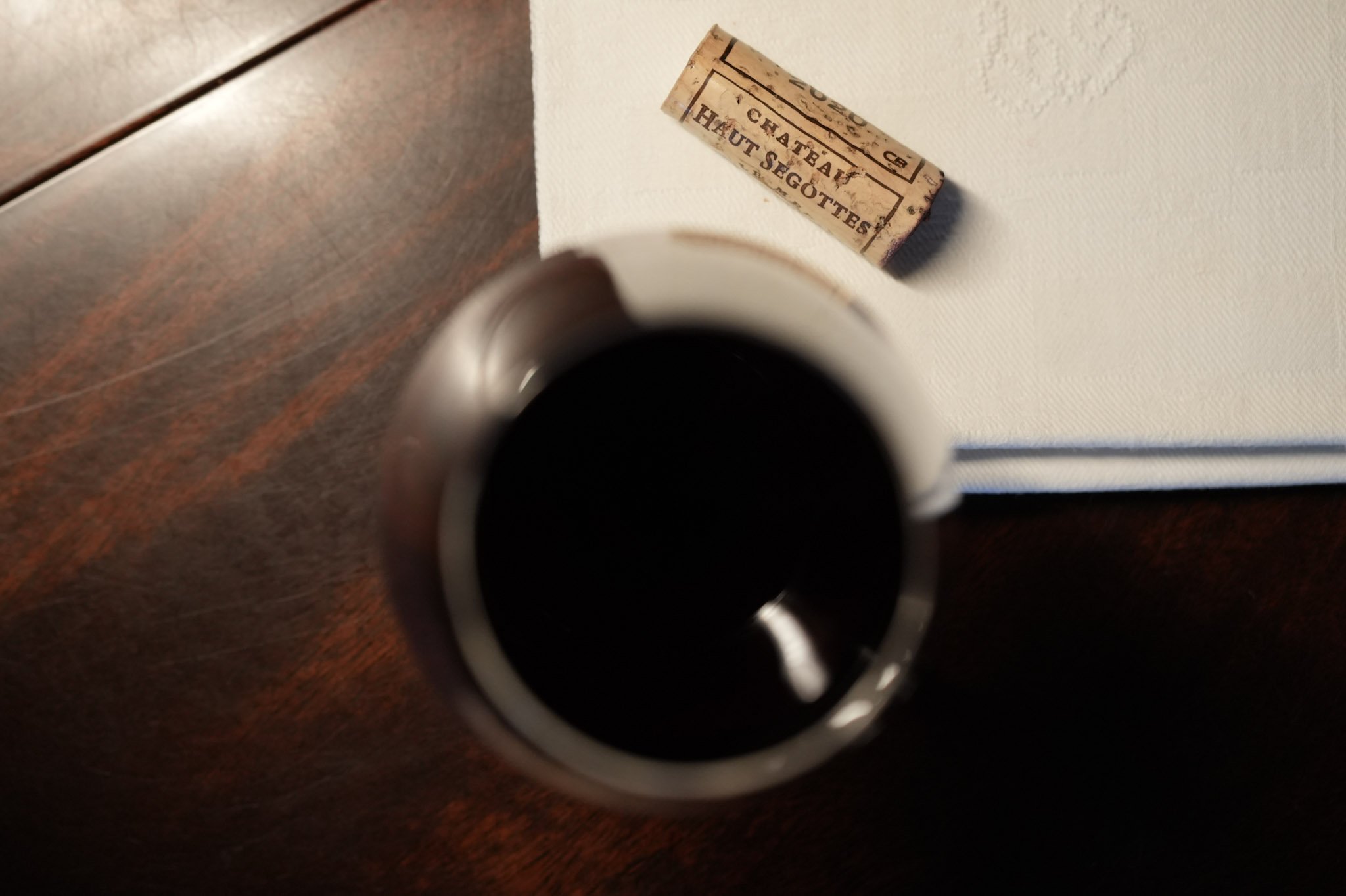 Une tasse de café noir vue du dessus, un livre à moitié visible avec une surface blanche, et une petite caisse en bois portant l'inscription 'CHATEAU HAUT SEGOTTES'.