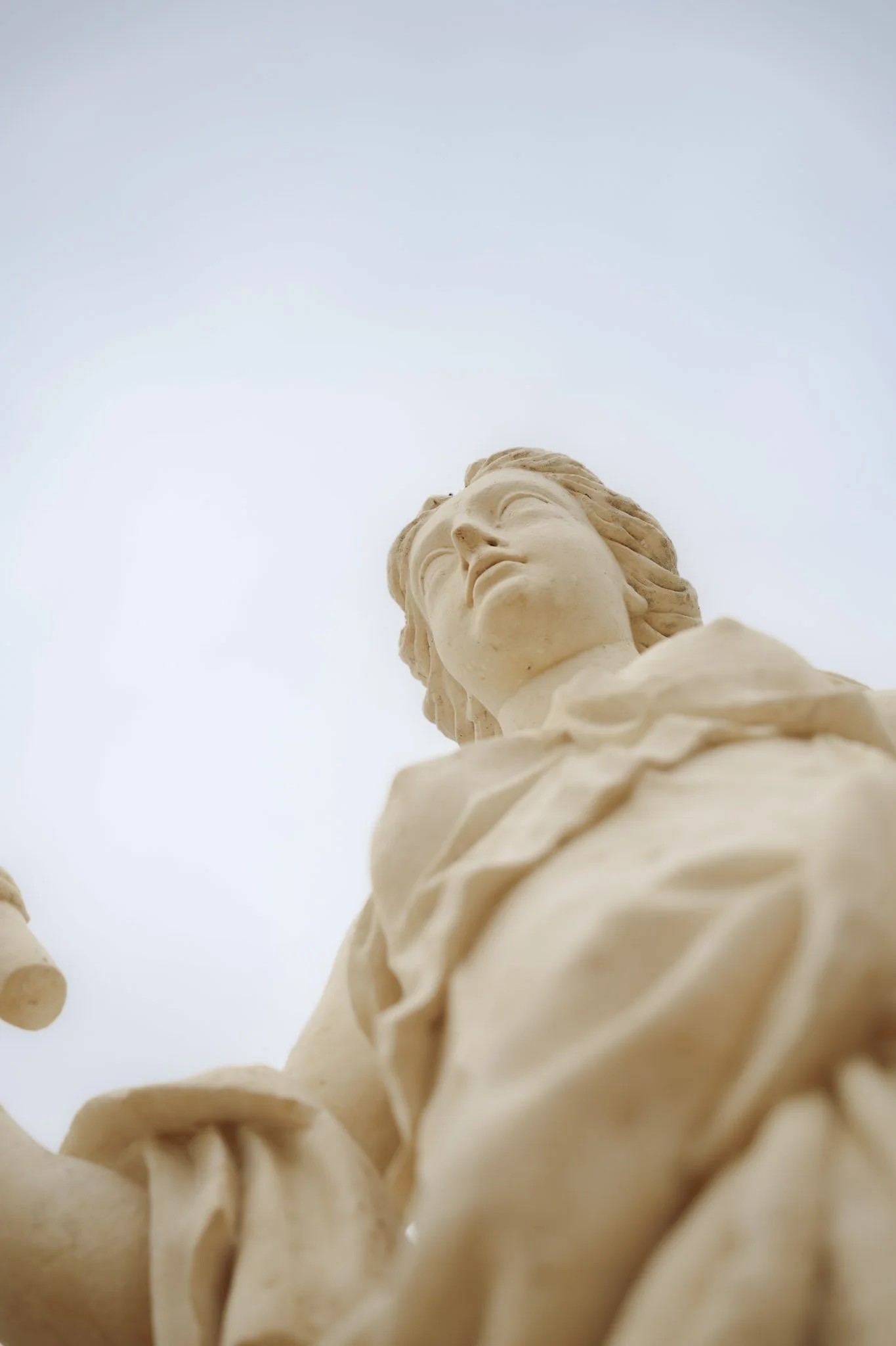 Statue en pierre d'une femme avec les yeux fermés, vue de dessous contre un ciel clair.
