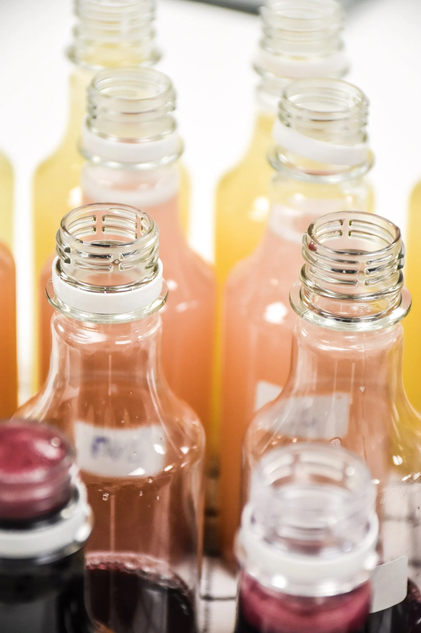 Bouteilles en verre colorées vides ou contenant des liquides, alignées sur une surface, avec un fond blanc.