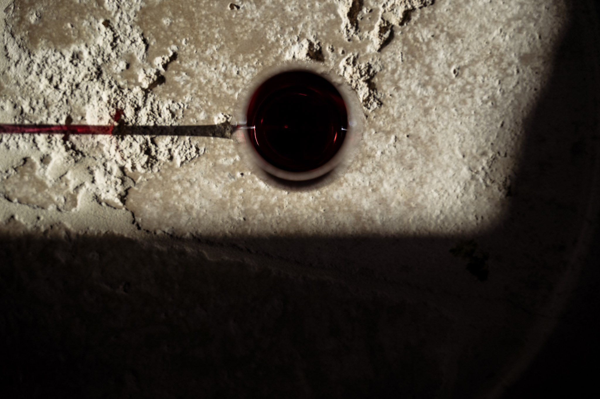 Une vue directement du dessus d'un trou d'évier ou de drain dans une surface de pierre ou de béton, avec un bout de tuyau ou de câble rouge à côté, en lumière tamisée.