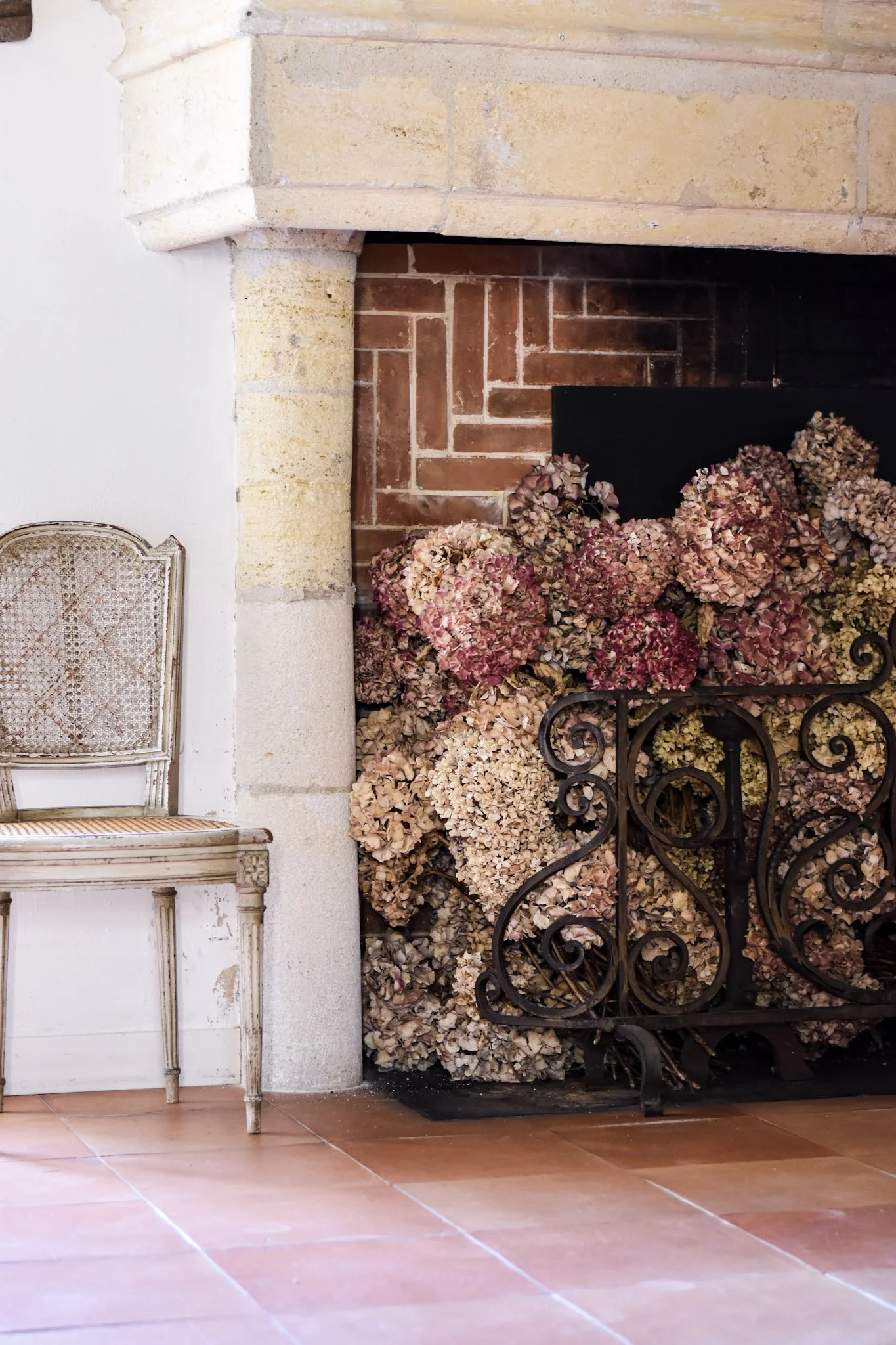 Floral arrangement with dried hydrangeas in front of a fireplace and an antique chair.
