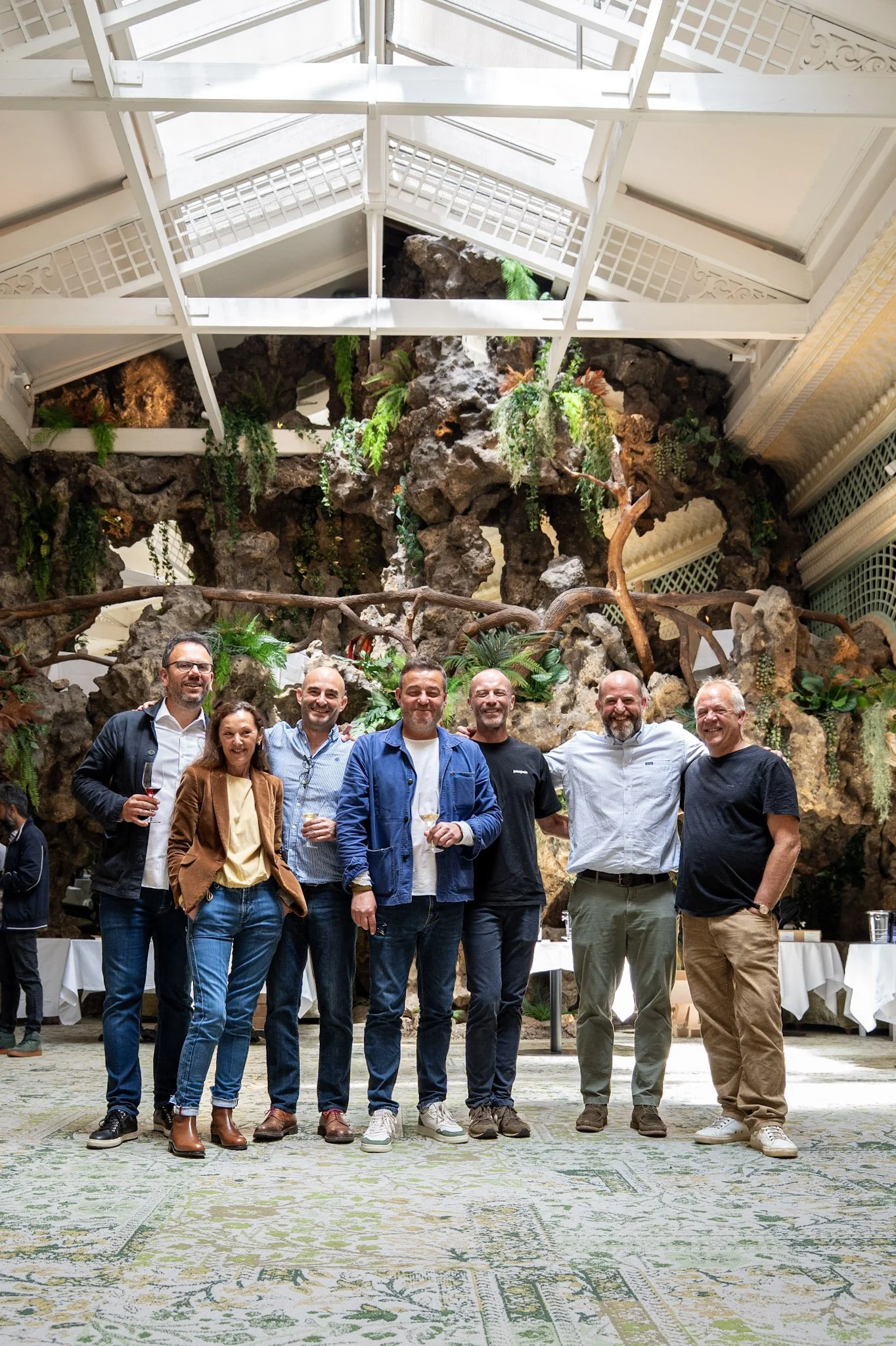 Groupe de huit personnes souriantes posant dans une salle élégante avec une grande fontaine végétale en arrière-plan.